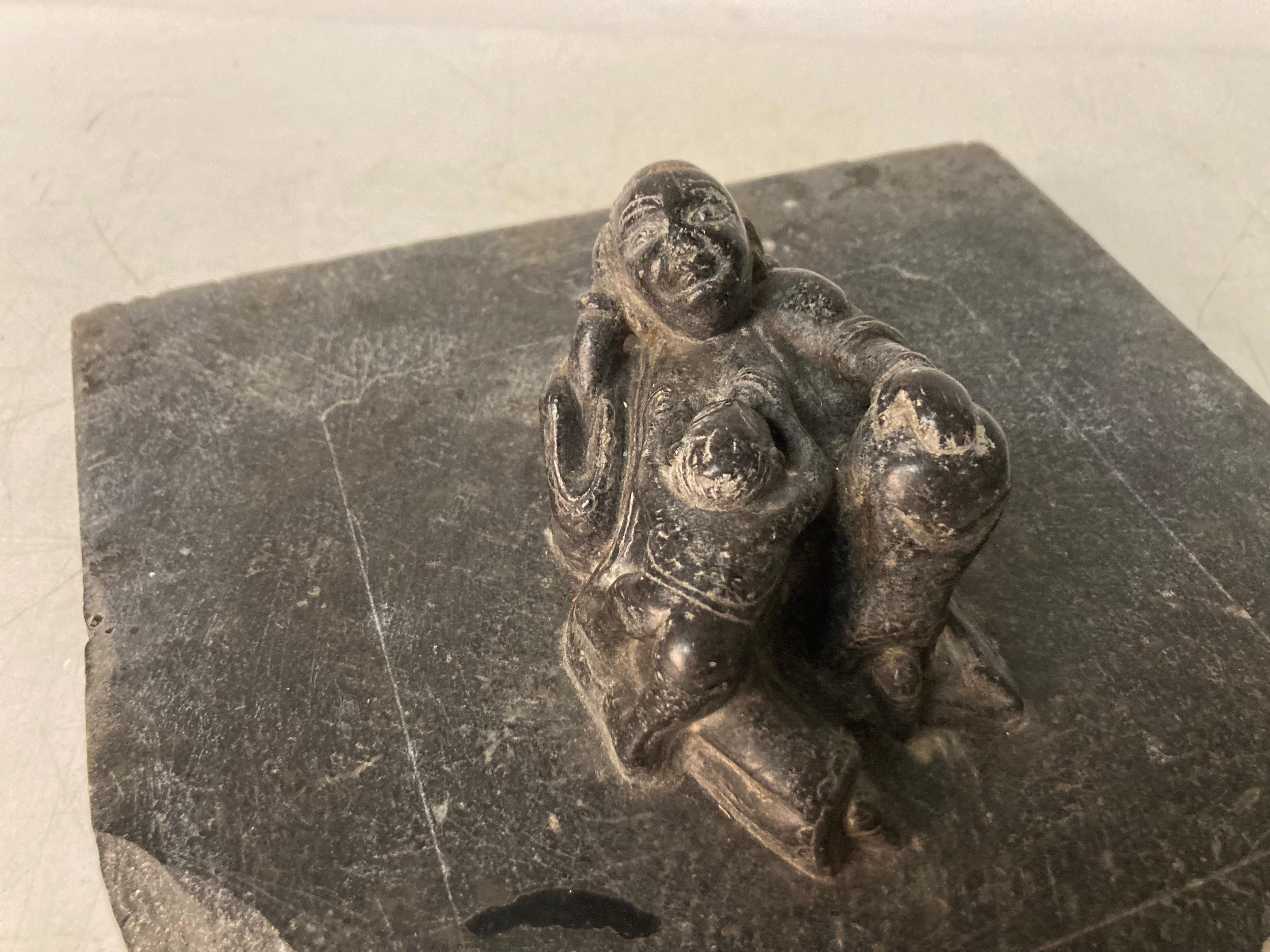 Una scultura in pietra da studio Inuit incompiuta che raffigura una Madre reclinata che allatta il suo bambino. La Madre con un'espressione serena e rivolta verso l'alto. L'intaglio, in pietra o ardesia grigio scuro con lucidatura morbida. Il pezzo