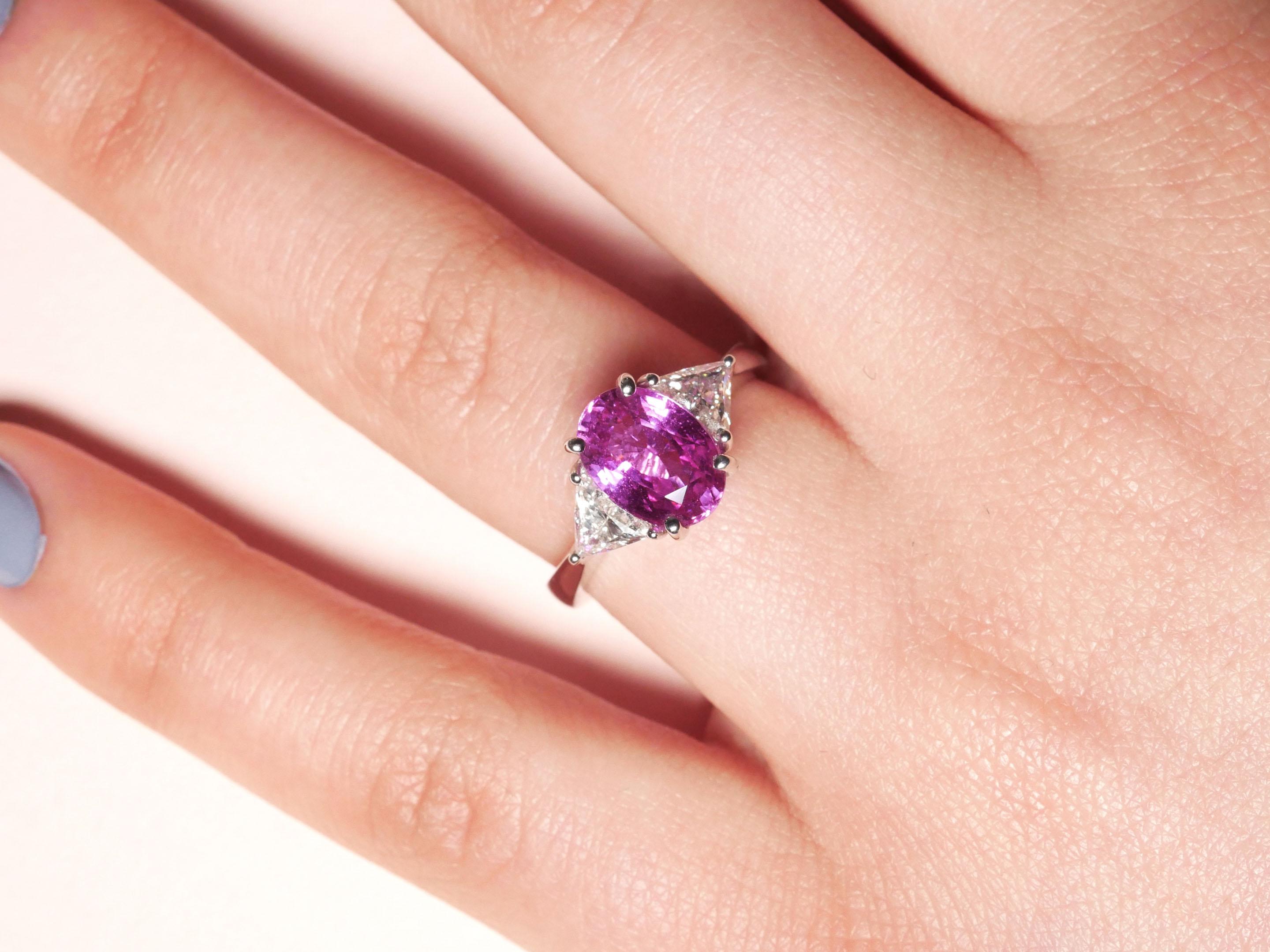 Make a statement with a piece that breathes new life into a classic three-stone ring. The centre stone is an oval sapphire in an intense pink hue, positioned between two triangular white diamonds that emphasize its rare colour. The stones are set on