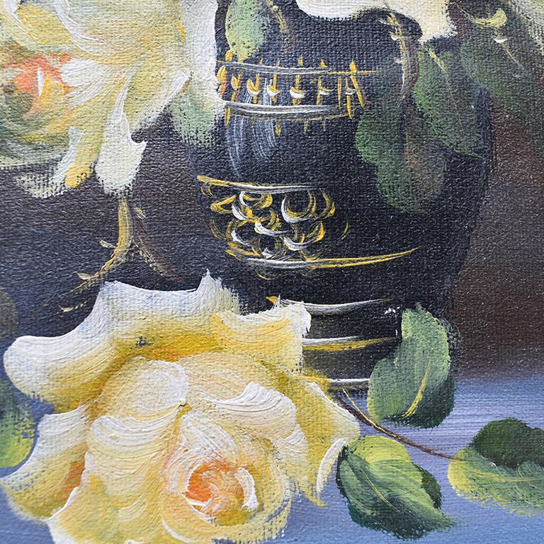 A pretty floral painting of a bouquet of flowers in a vase. This piece features creamy white flowers with accents of yellow. The roses sit in a black neoclassical style vase upon a blue tablecloth. 

Dimensions:
13