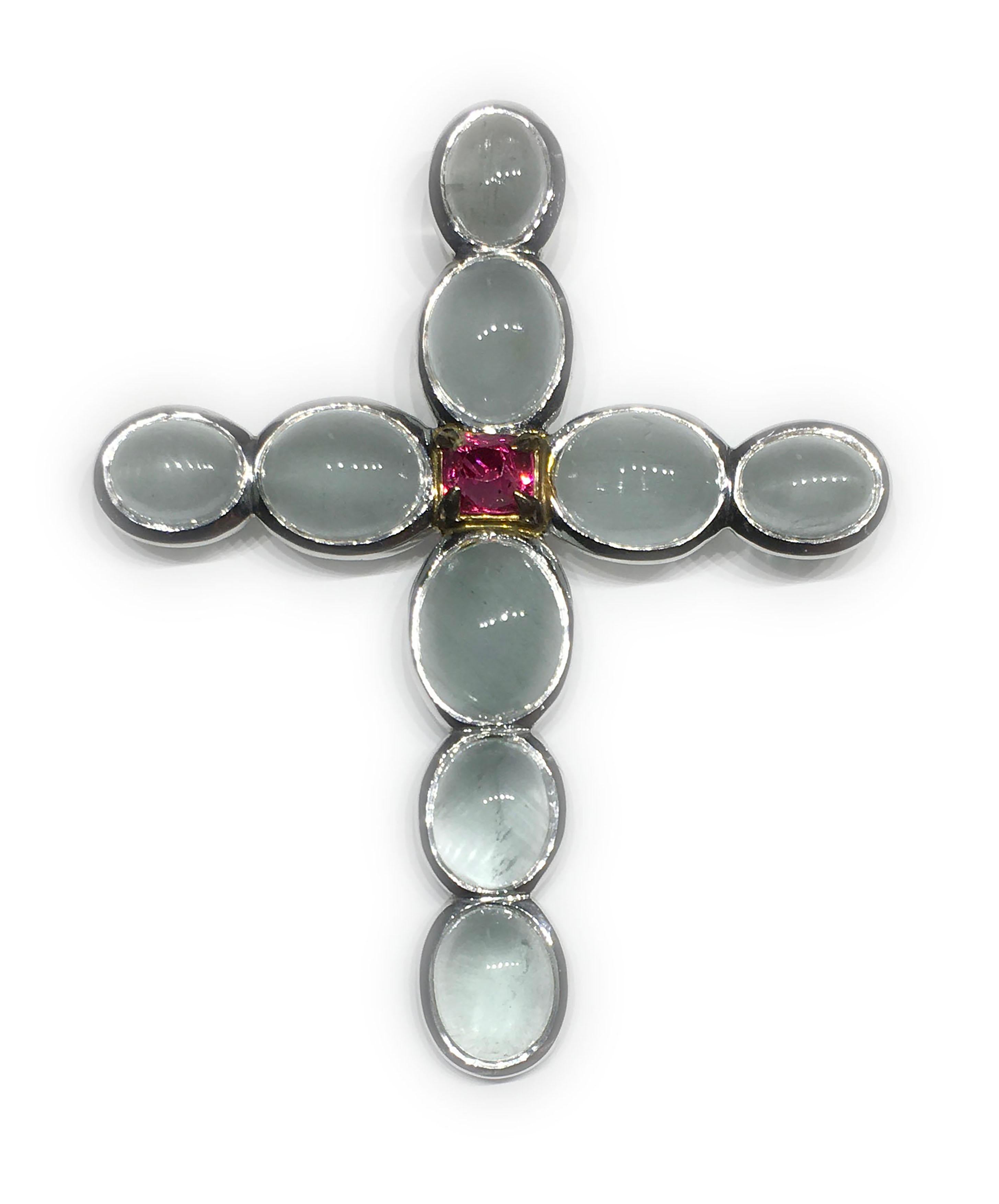 A Sterling Silver Cross Pendant set with 10 Brazilian, Milky Aquamarine Cabochons and a vivid Pink Natural Untreated Sapphire. Milky Aquamarine Cabochons total 32.8 Carats, The Natural Sapphire is  1.55 Carats. Silver Weight 15.45 Grams.

Originally