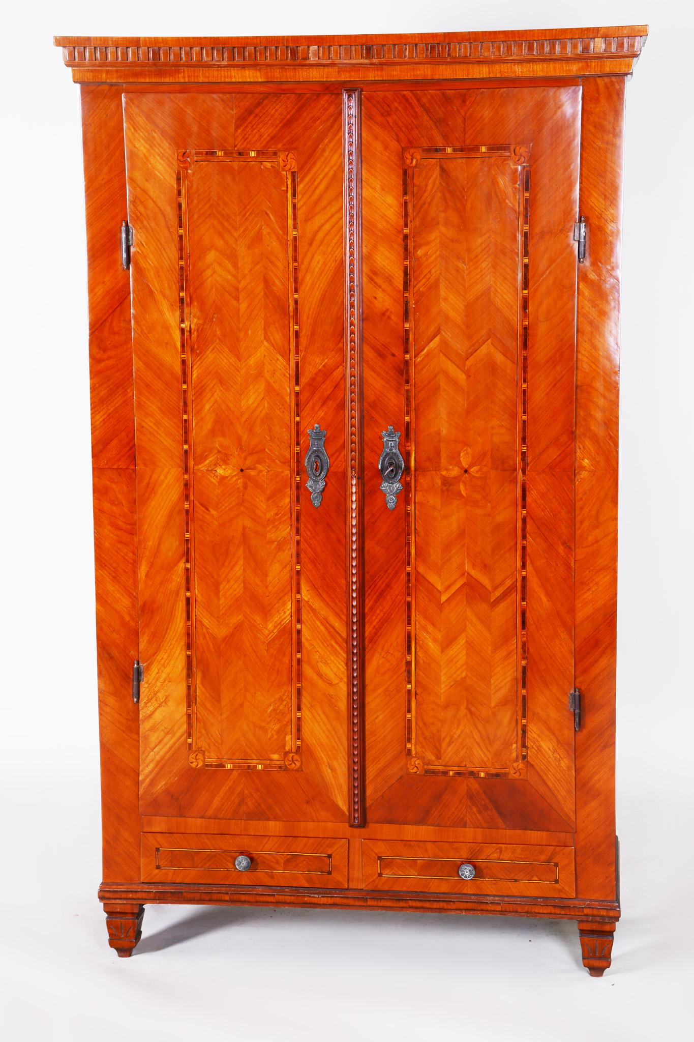 Exceptional classicist castle wardrobe. Very well-preserved and completely authentic with two drawers, decorated with marquetry and a typical classicist vaulting of the upper ledge and legs.

18th century classicist double-door wardrobe
Completely