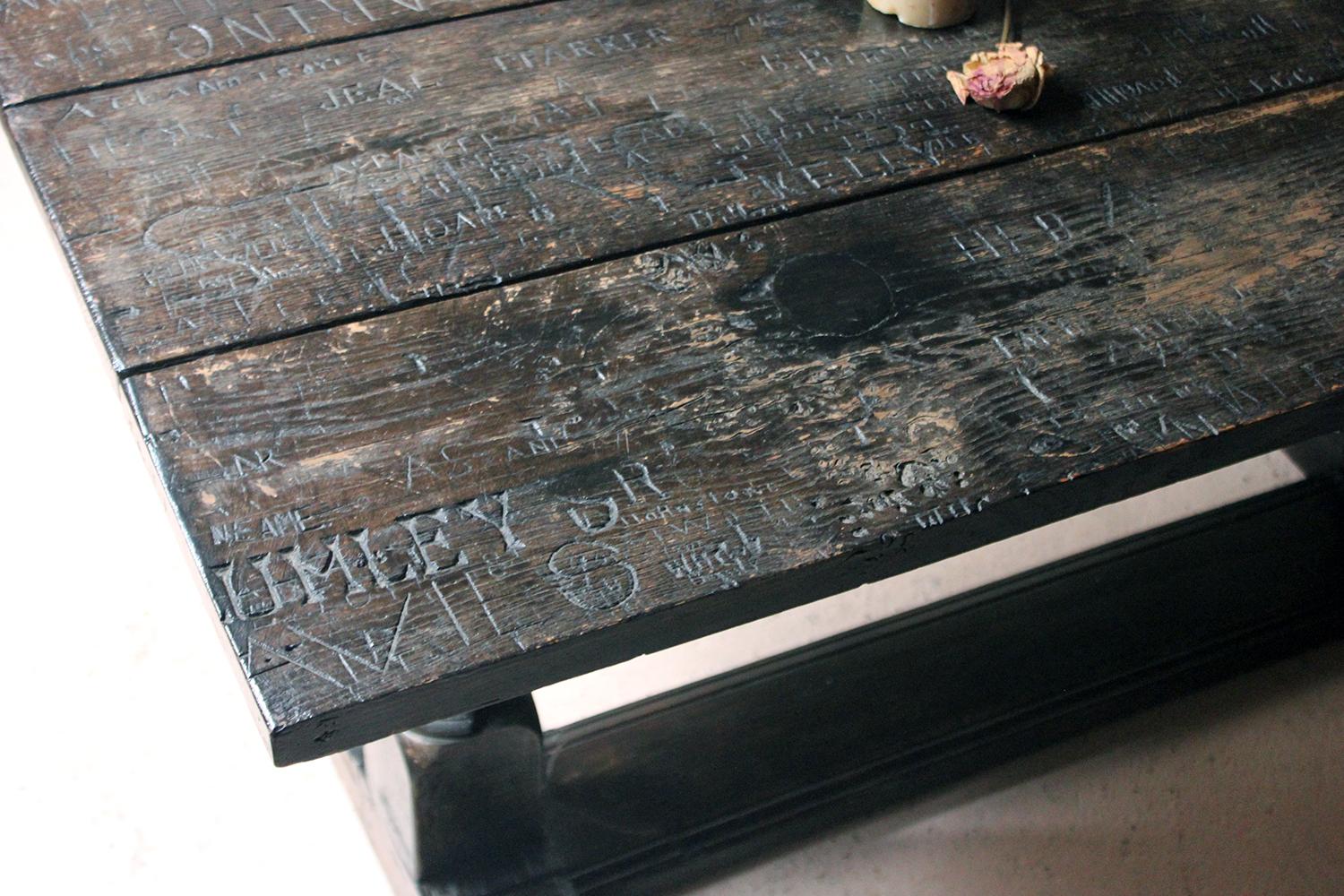 The unusual oak refectory table having a three-plank top with extensive chiselled graffiti, with names and initials of numerous English school boys, the earliest date at 1873 through to 1897, the later married base having turned baluster trestles,