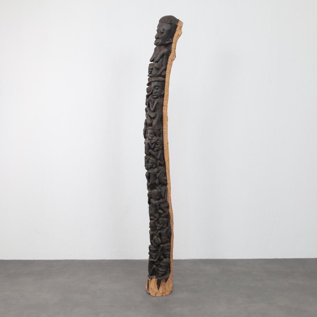 Un alto tótem de madera tallado a mano, rico en significado simbólico y artesanía. Esta escultura única representa una procesión vertical de figuras humanas, cada una intrincadamente tallada con gestos expresivos y presencia espiritual. Tótems como