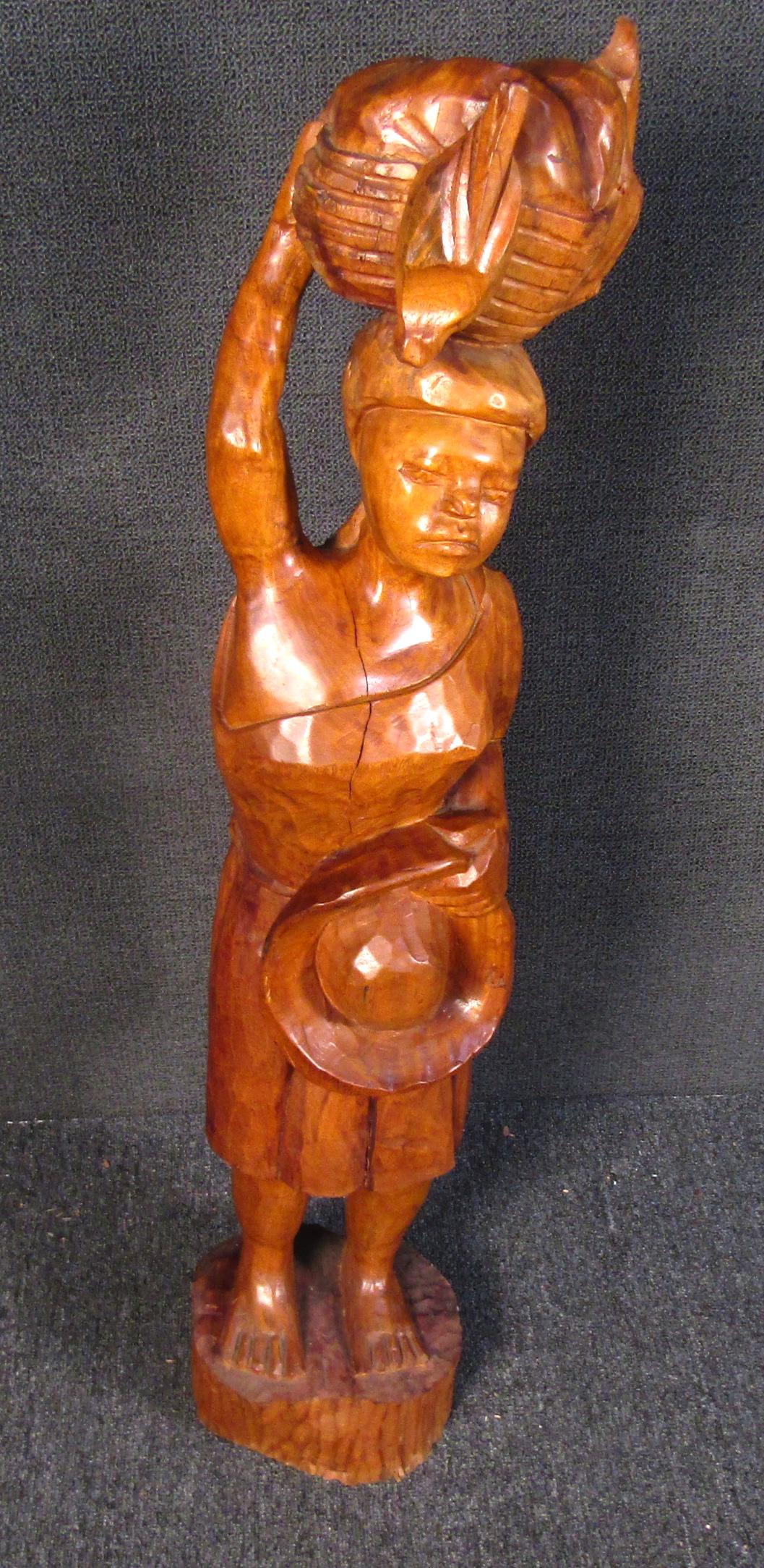 Beautiful one of a kind African carved wooden sculpture of a woman carrying a basket and a hat. Featured in a rich warmly stained wood, this stunning hand carved sculpture will surely be a statement piece among any collection of art.

Please confirm