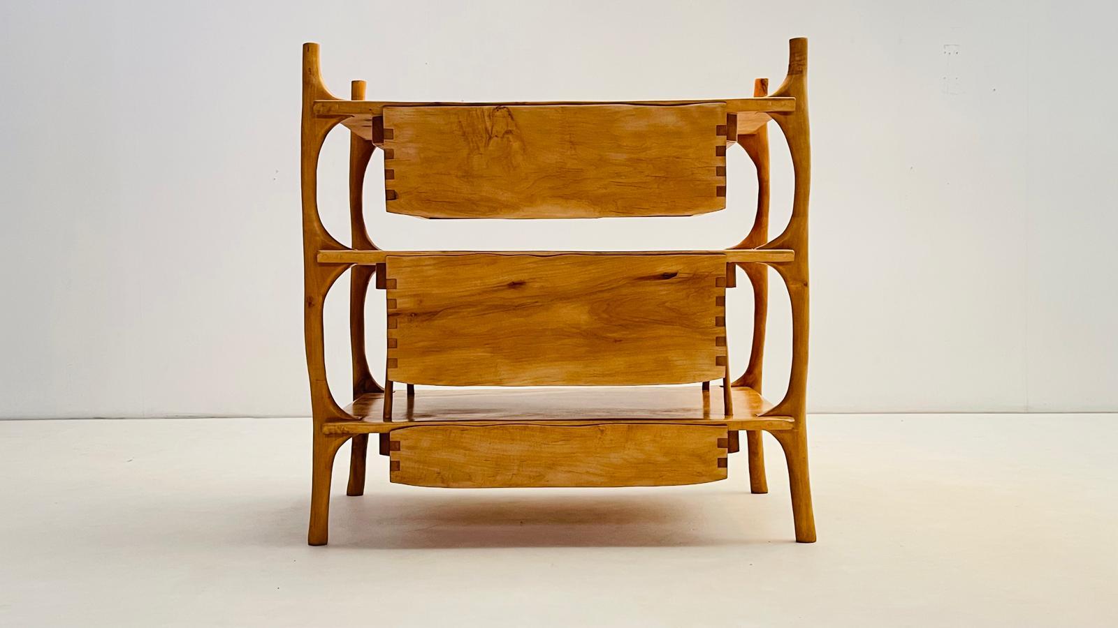 This chest of drawers stands out for its sculptural, almost skeletal wooden frame, which supports three floating drawers. The structure is entirely hand-carved, with softly rounded edges following the natural fibers of the wood plates. 

This light