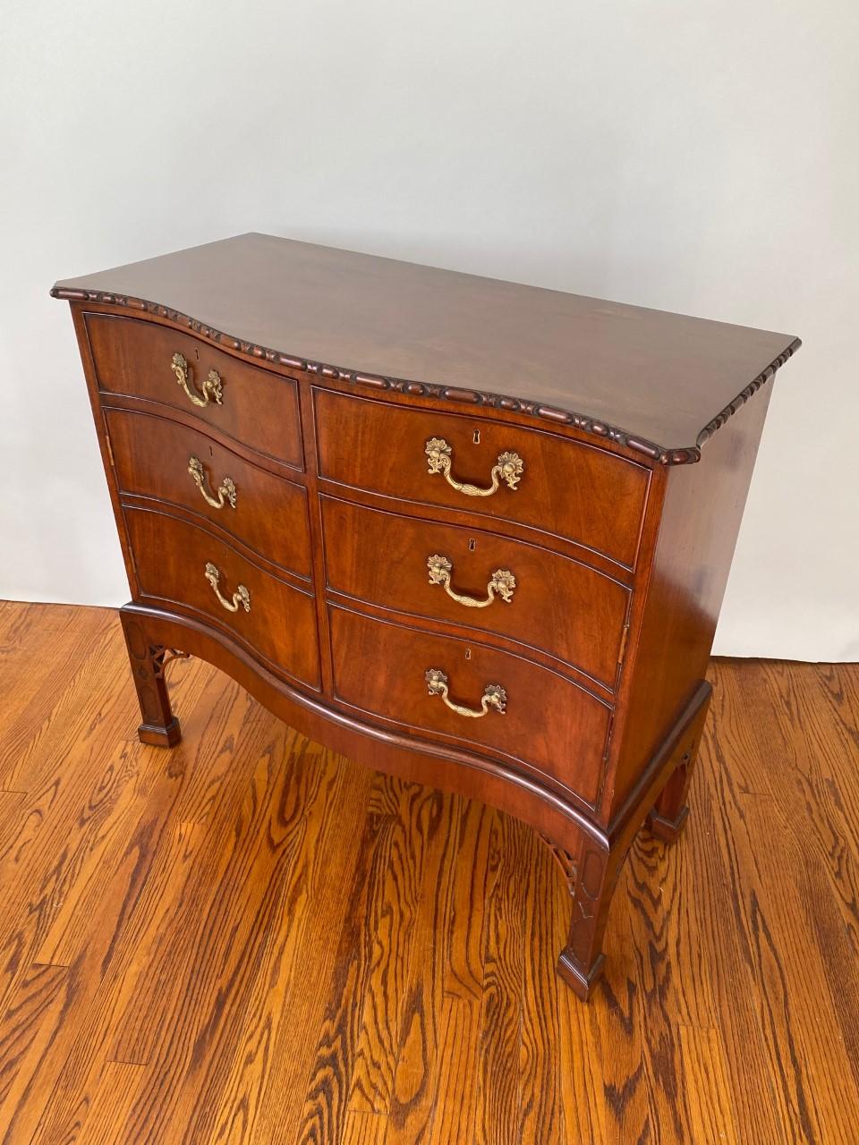 The unique and handsome English-made Chippendale style serpentine front commode on stand is made from selected Mahogany and is exquisitely carved by hand. The top two fitted box drawers are active; underneath them are false drawers concealing a