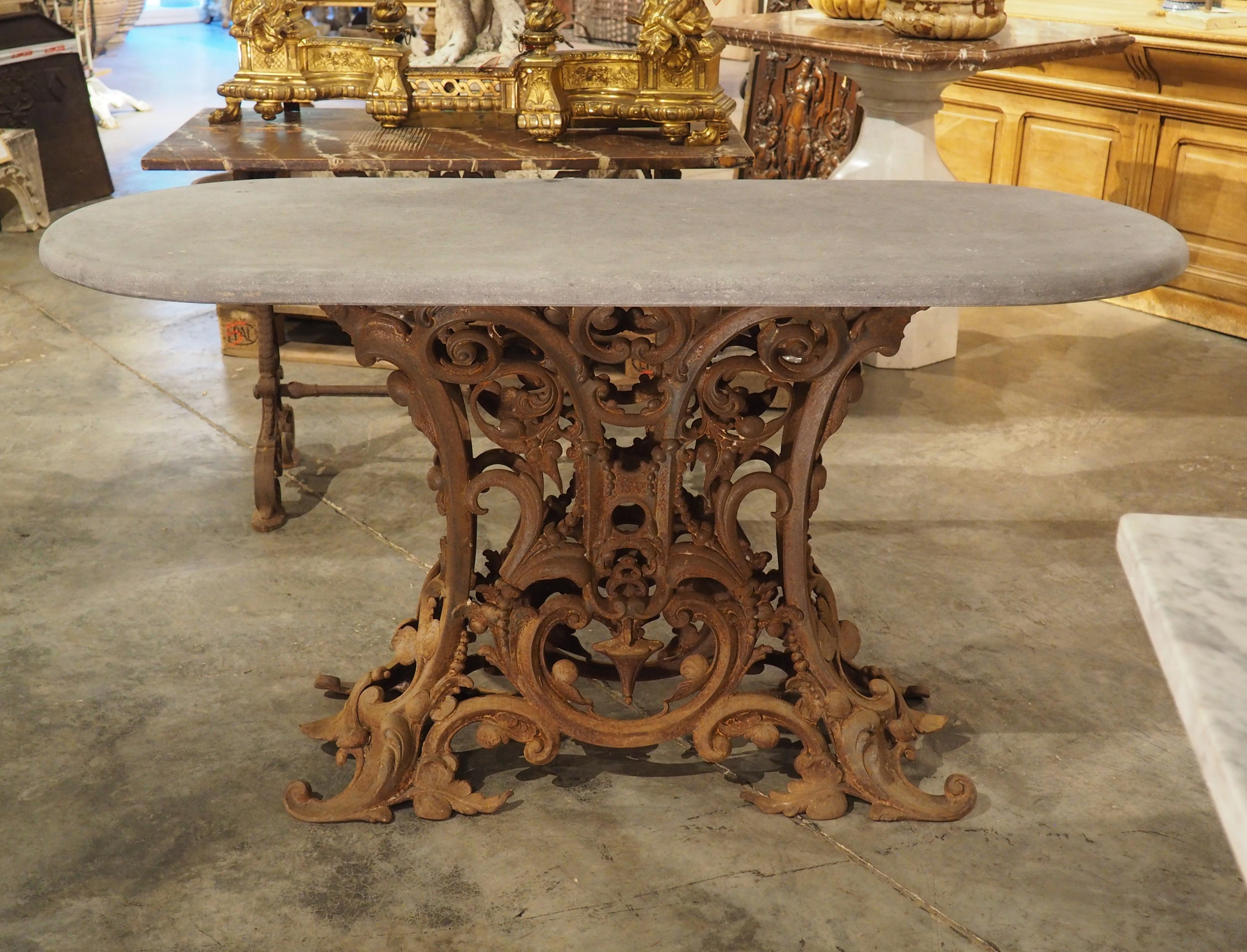 Dating to circa 1900, this unique French table has an oval bluestone supported by a robust cast iron base. The base is comprised of an elaborate foliate margent intertwined with scrolls, beading, and rinceaux. Traces of the original gray finish can