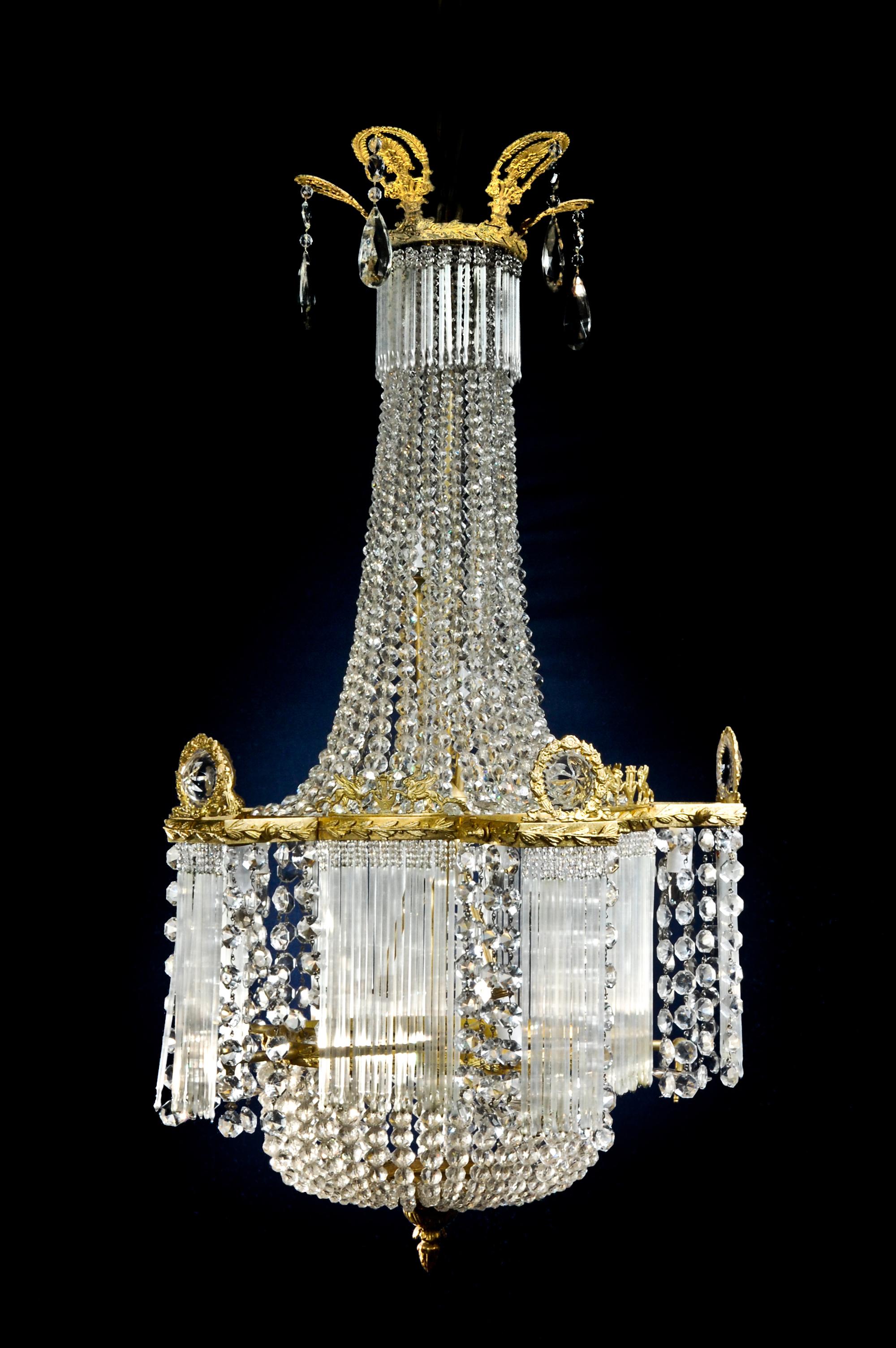A unique antique French Louis XVI style multi-light gilt bronze and cut crystal multi light chandelier of unusual form embellished with cut crystal prisms, chains and further adorned with gilt bronze mounts depicting neoclassical griffins with