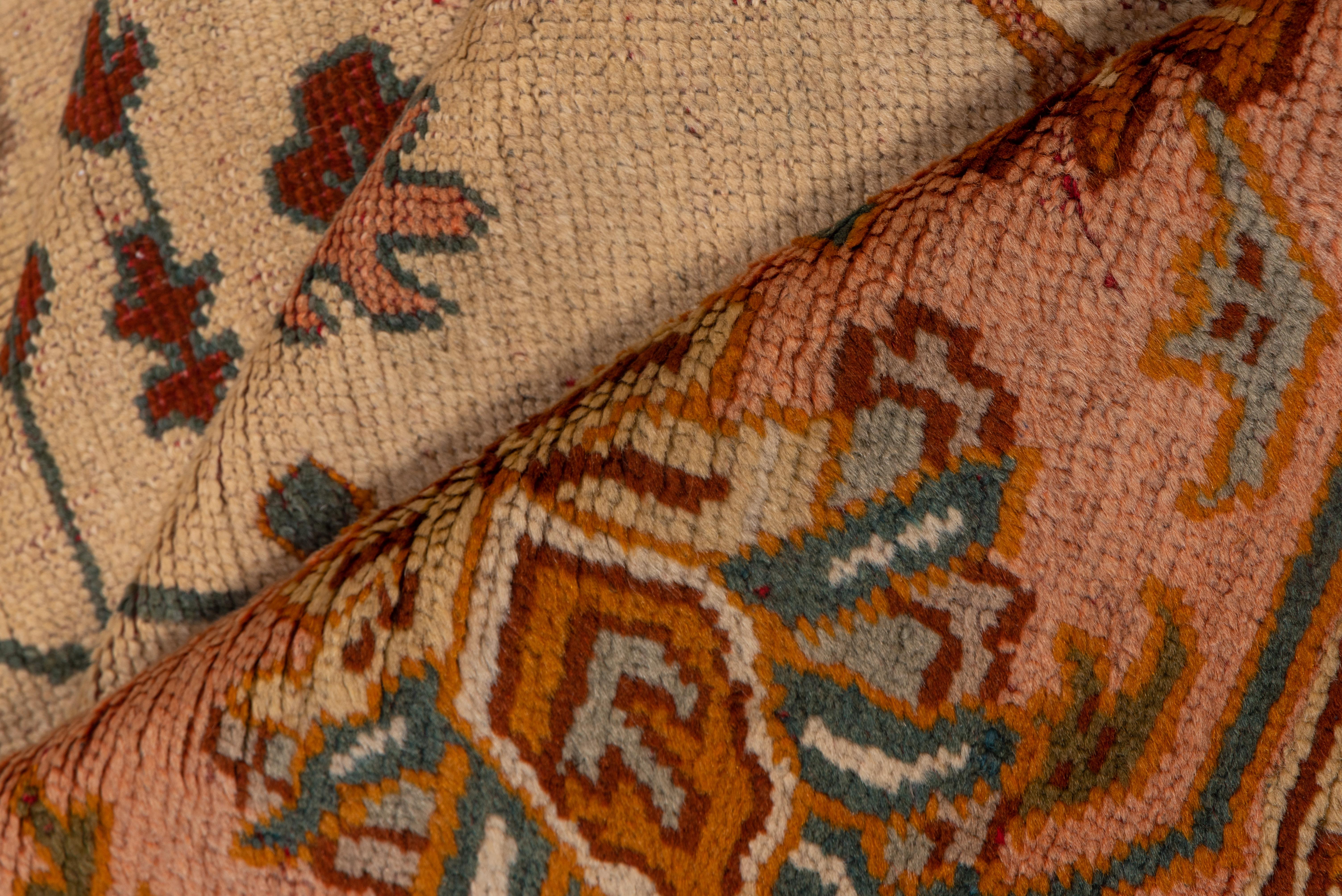 Le fond crème de ce joli tapis d'atelier d'Anatolie occidentale présente un vaste motif de palmettes dentelées, de rosettes de pétales et de vignes épaisses, centré par un motif cruciforme complexe, le tout en vert ivoire, rouille, chamois et