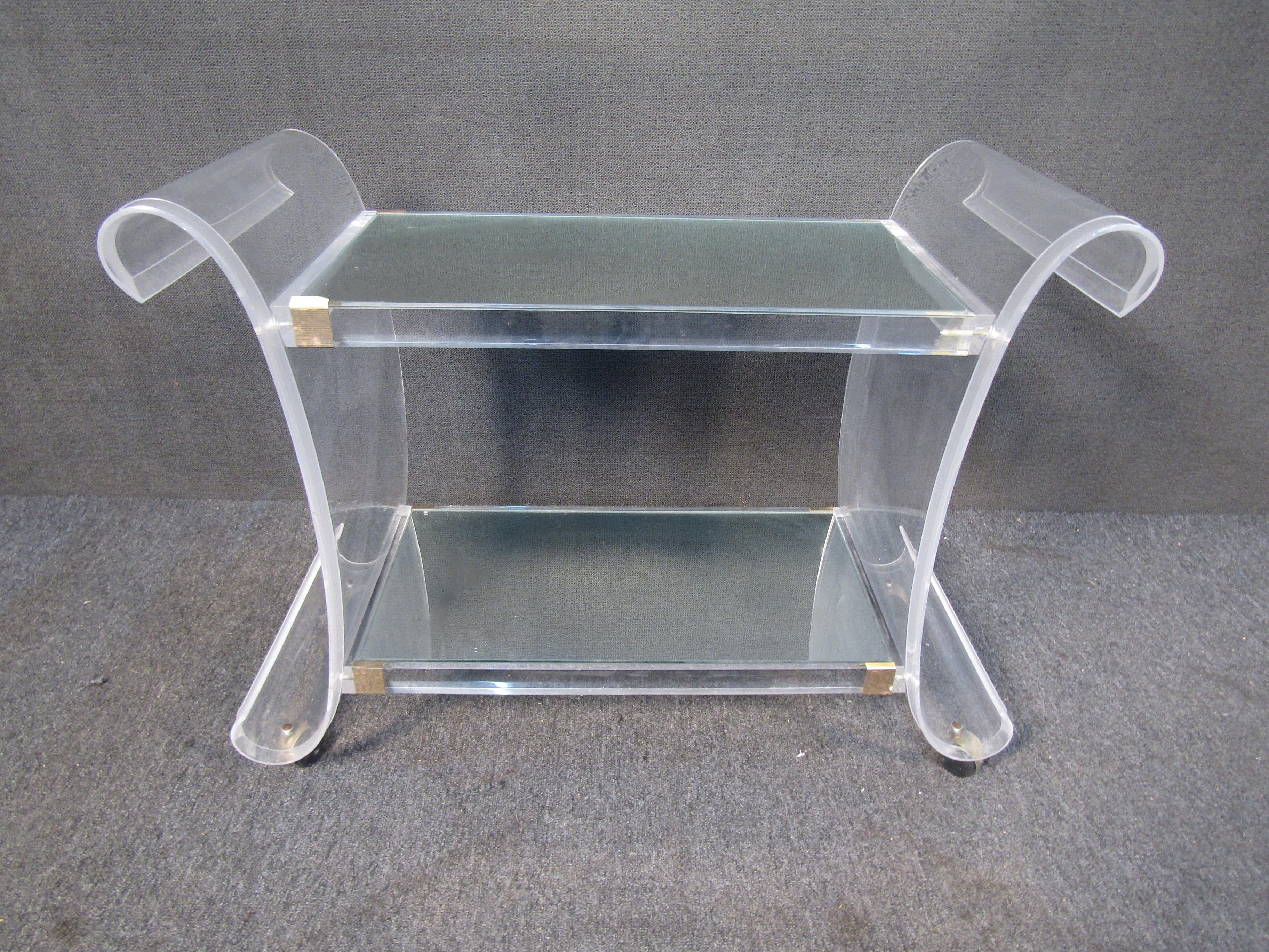 With a very unique curving lucite frame, metal accents, and a mirrored top, this two-tiered bar cart is an eye-catching addition to any kitchen or interior. Please confirm item location with seller (NY/NJ).