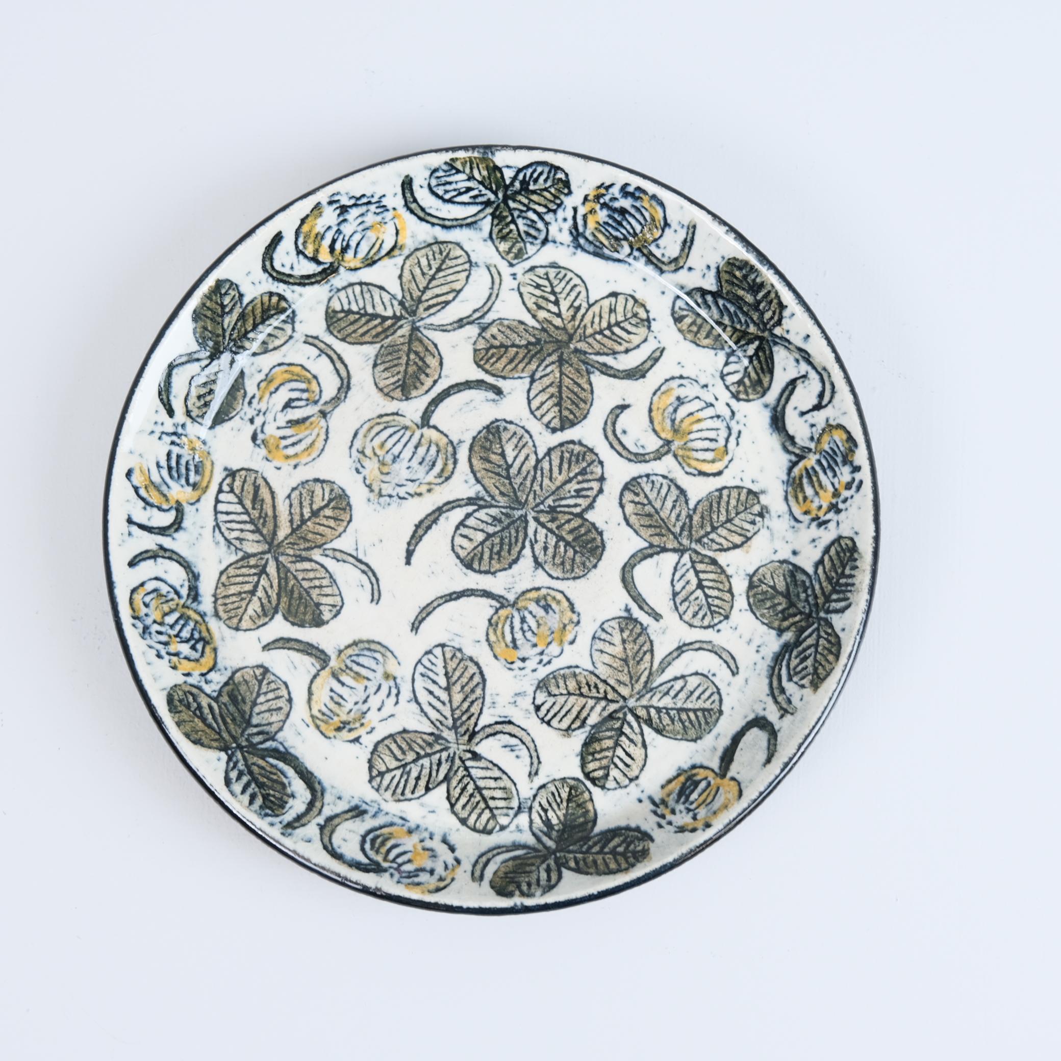 A beautiful small and unique ceramic plate designed by Birger Kaipiainen for Arabia in Finland in the 1970s. The plate is decorated with multiple four-leaf clovers, three-leaf clovers, and flowers, creating a charming and whimsical design. Though