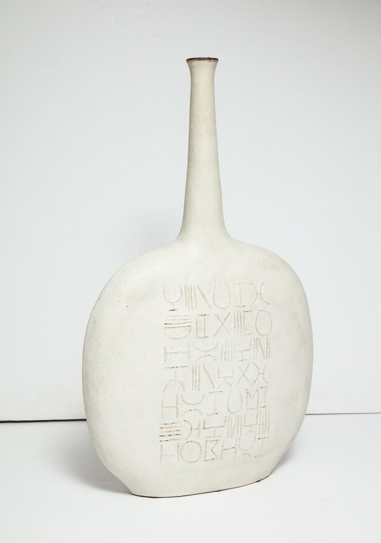 Large scale stoneware bottle form sculpture/vase with incised line decoration to front and
back faces. Off-white matte glaze with brown lip. Artist signed at base.