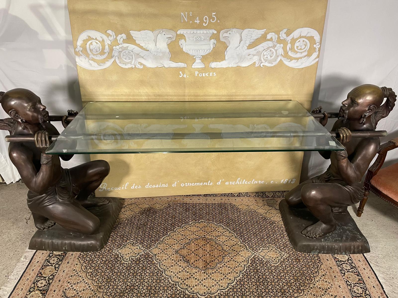 Cette exceptionnelle table d'appoint en bronze du début du XXe siècle est un véritable chef-d'œuvre de design et d'artisanat. La table présente deux personnages masculins sculptés de manière complexe, chacun portant sur ses épaules des tiges de