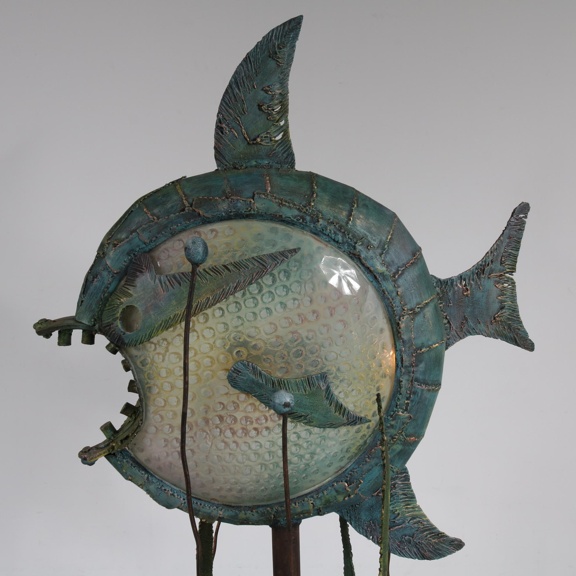 This impressive floor lamp in Brutalist style was produced in the Netherlands, circa 1960.

It is made of different shades of metal, copper and clear synthetics. It is shaped like a big fish, including metal kelps going up from the foot, which
