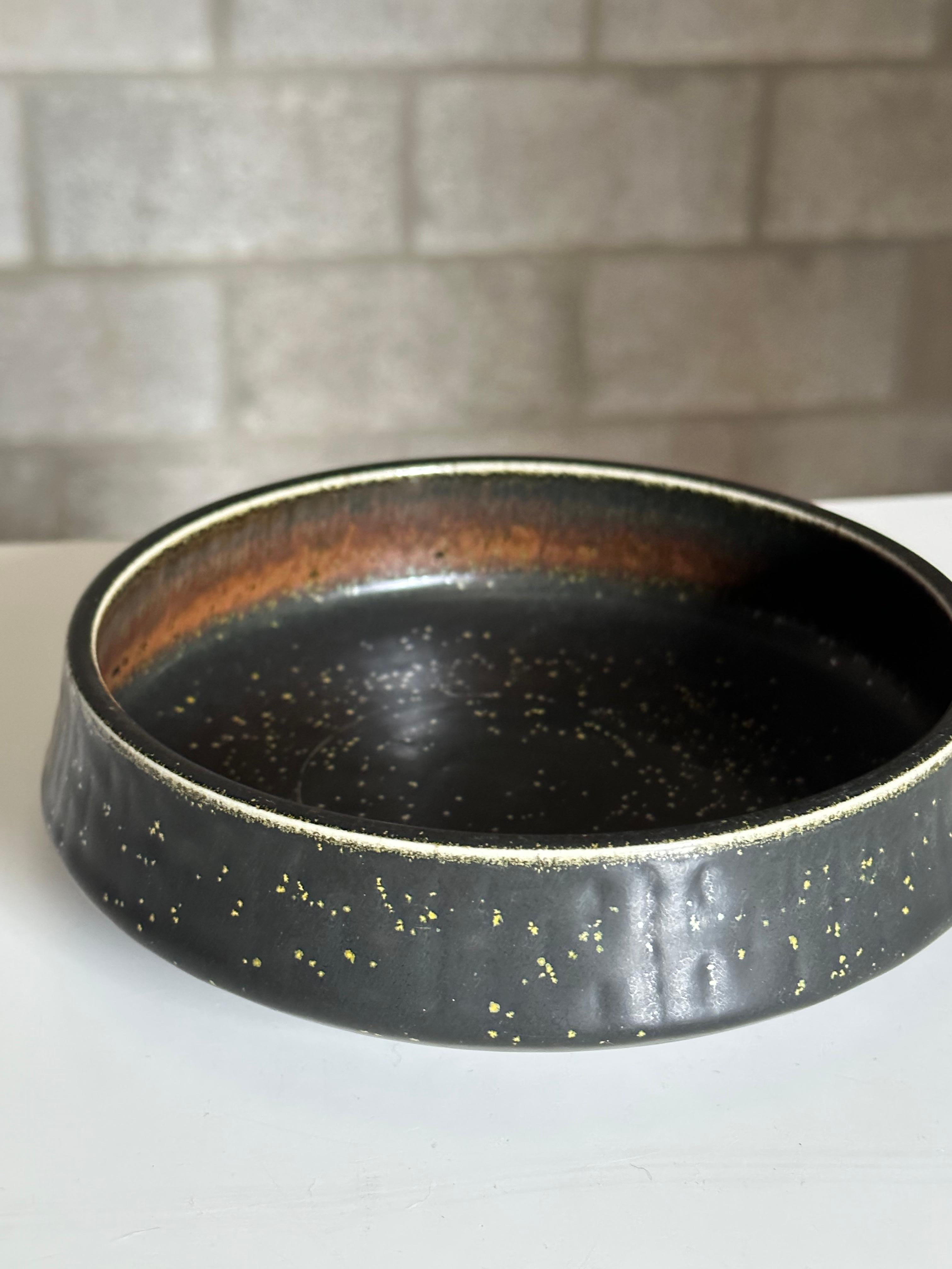 A unique bowl designed by Carl Harry Stålhane for Rörstrand. Bowl features a dramatic dark almost black glaze with speckles. The inside has hues of dark brown transitioning to light brown around the rim.