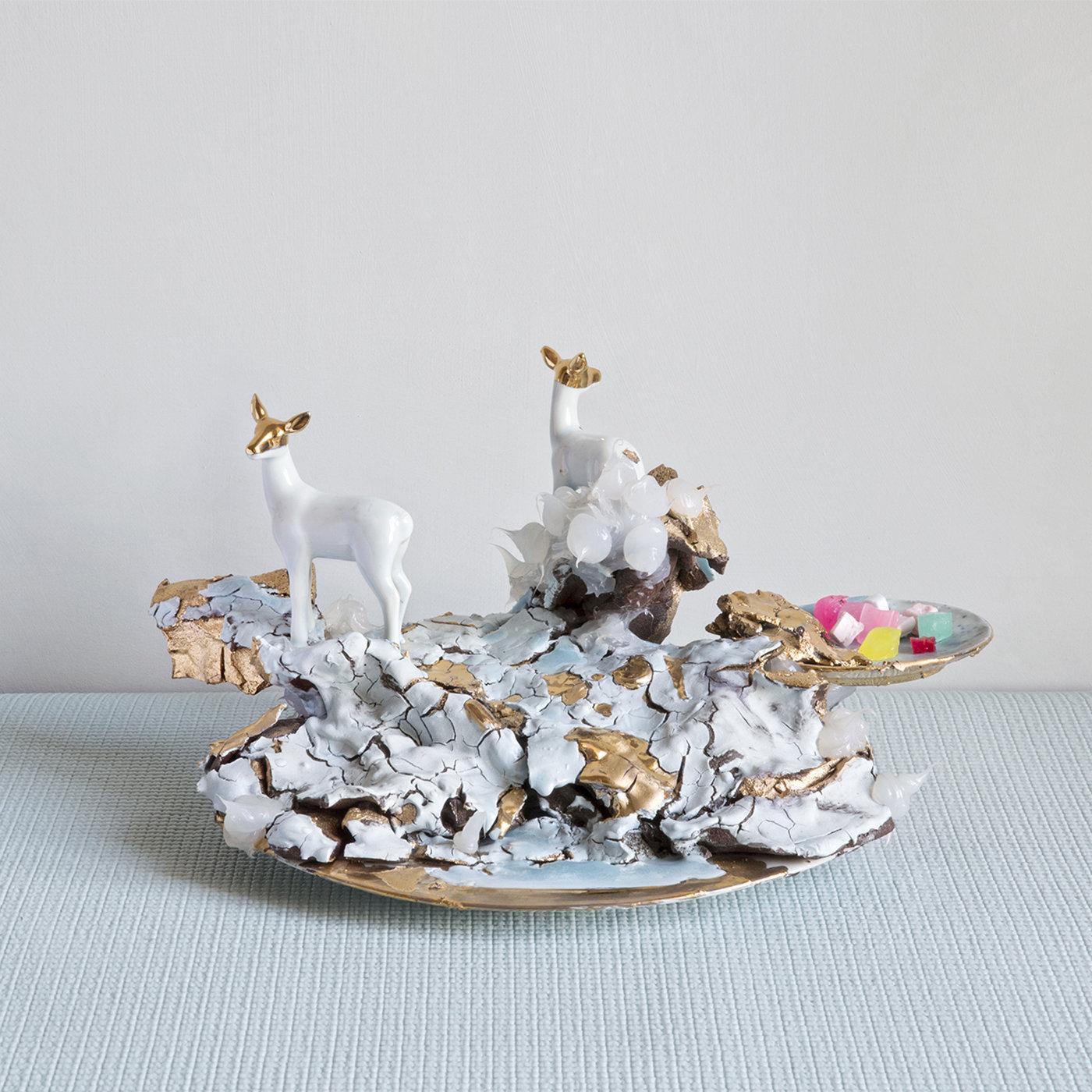 Two small white animals stand looking at their surroundings on a mound of cracked earth in pale blue and gold. These pieces are made by experimenting in total freedom, with the addition of silicone, crystals, porcelain animals and some small