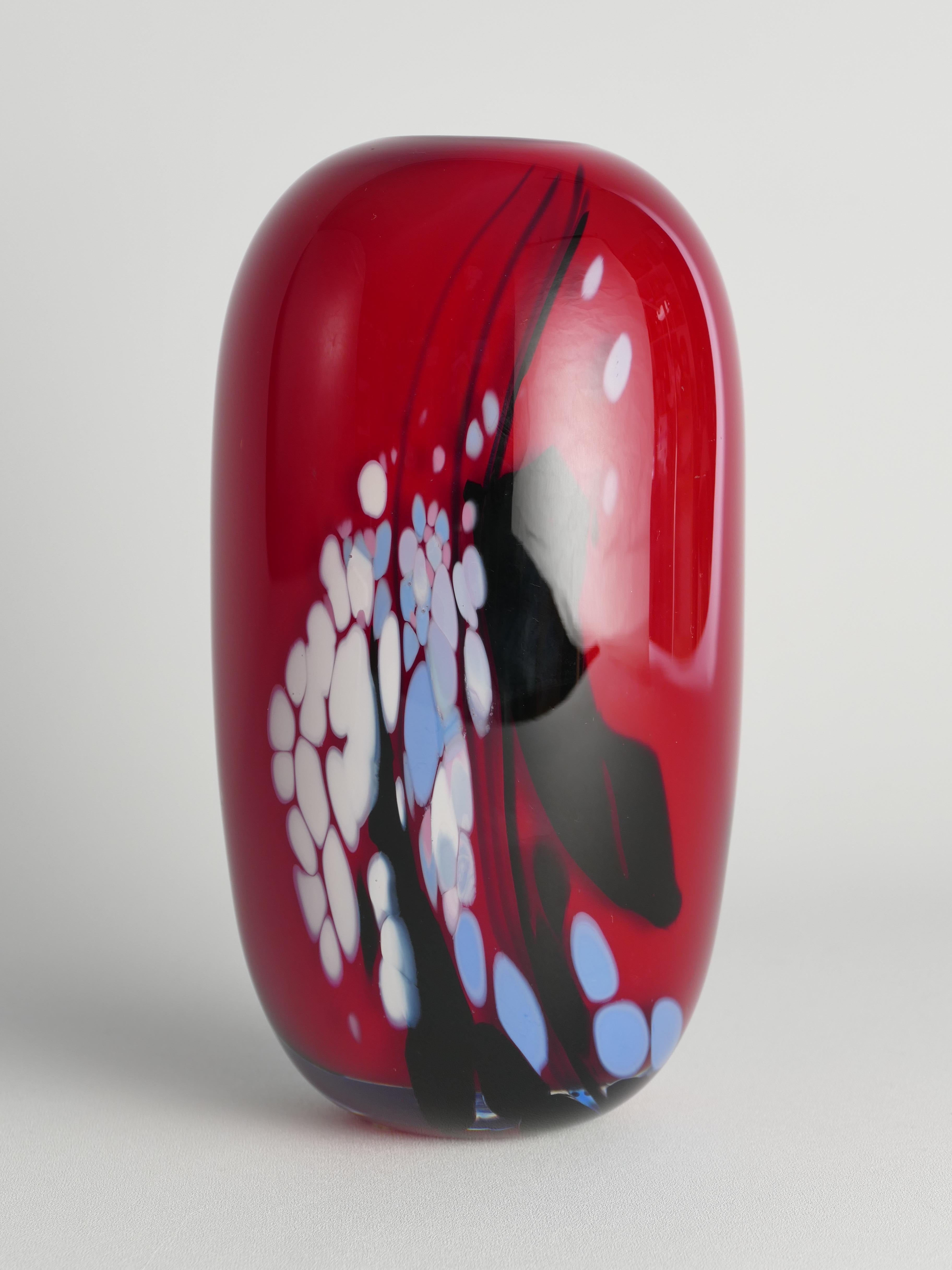 Diese schwere, elegante und farbenfrohe Vase aus Kunstglas wurde 1990 von dem Glasmeister Mikael Axenbrant hergestellt. Glänzend rot wie eine zarte Kirsche mit blauen, weißen und schwarzen Strichen und Punkten.

Eingraviert: 