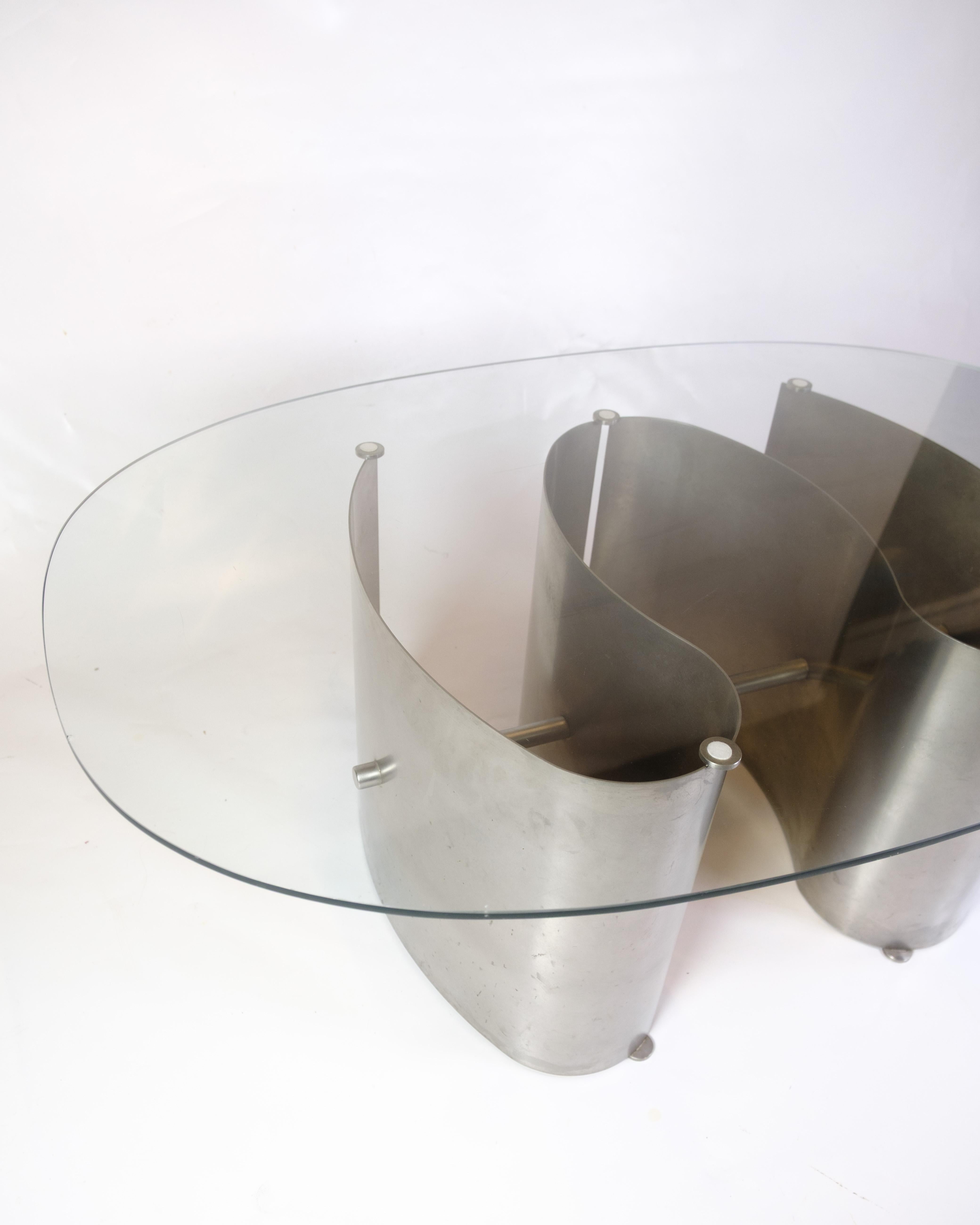 Tavolino scultoreo con vetro trasparente e struttura in acciaio saldato a mano, firmato J. Flemmer 3.9.1986. Il tavolo è un pezzo unico, progettato e realizzato da Jørgen Flemmer, noto per il suo design architettonico e grezzo in metallo e vetro. Un