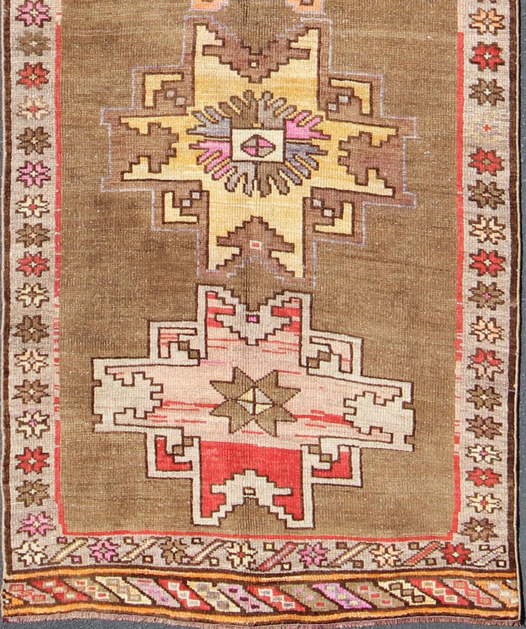 Vintage Turkish runner in greenish Brown background, ivory border with accent colors, red, pink, tan, green, bright yellow, taupe, rug/TU-UGU-4806, country of origin / type: Turkey / Oushak, circa 1940

This vintage runner features an assortment