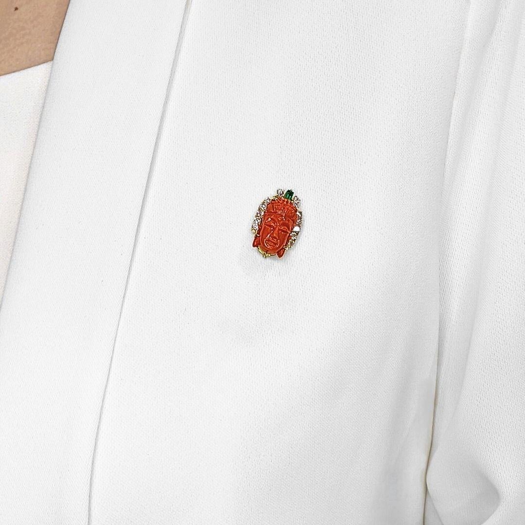 Kühn, künstlerisch und reich an Erbe, ist diese  Brosche mit einer meisterhaft geschnitzten orange-roten Koralle in der Mitte, gefasst in leuchtendem 14-karätigem Gelbgold. Die 14 natürlichen Diamanten - 12 runde Brillanten (0,42 ct) und 2 spitz