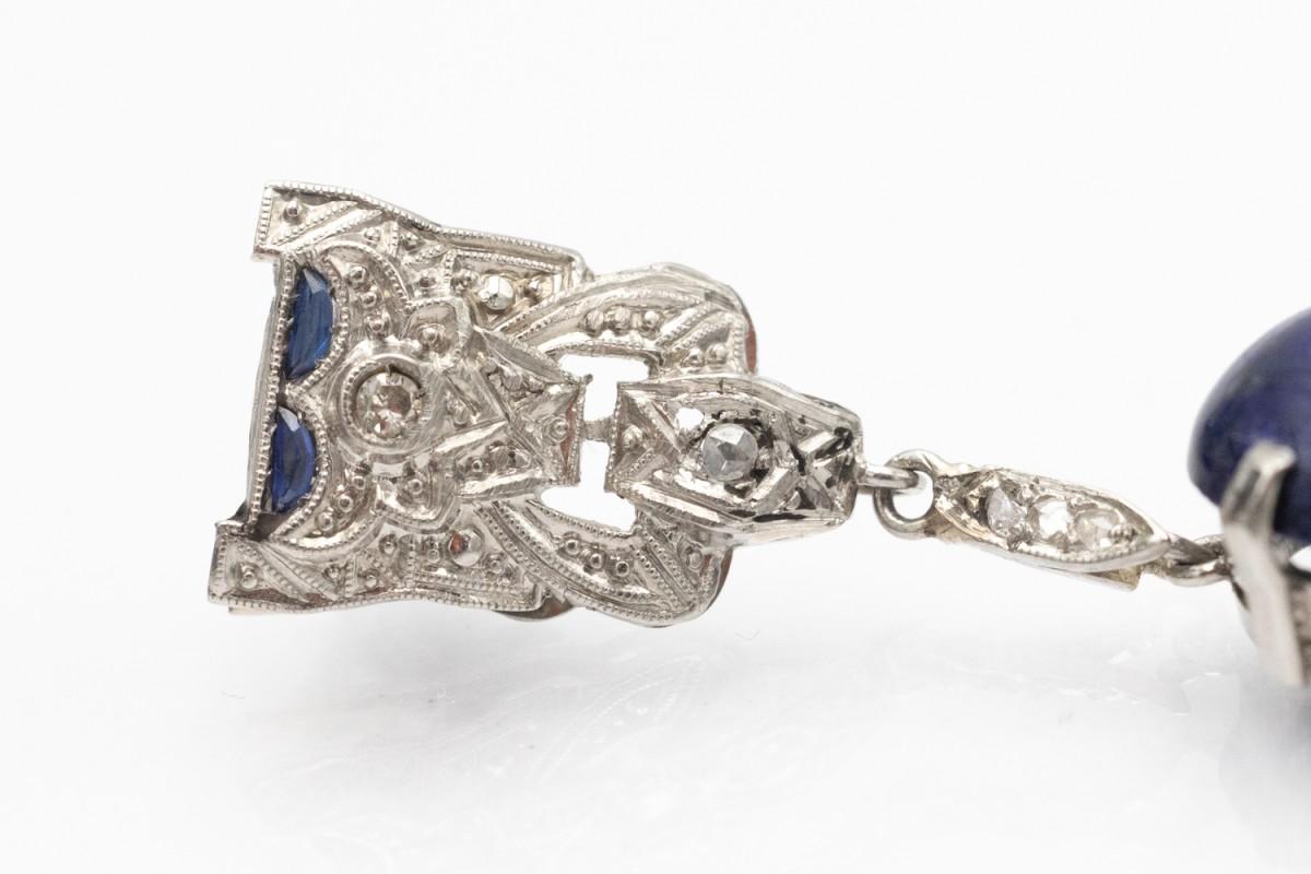 Boucles d'oreilles pendantes de style Art déco en platine 0,900.

Décoré de magnifiques cabochons de lapis-lazuli d'un bleu profond et de dimensions 20x15x5mm.

Le pendentif est orné de diamants taillés en rose et de saphirs synthétiques.

Origine :