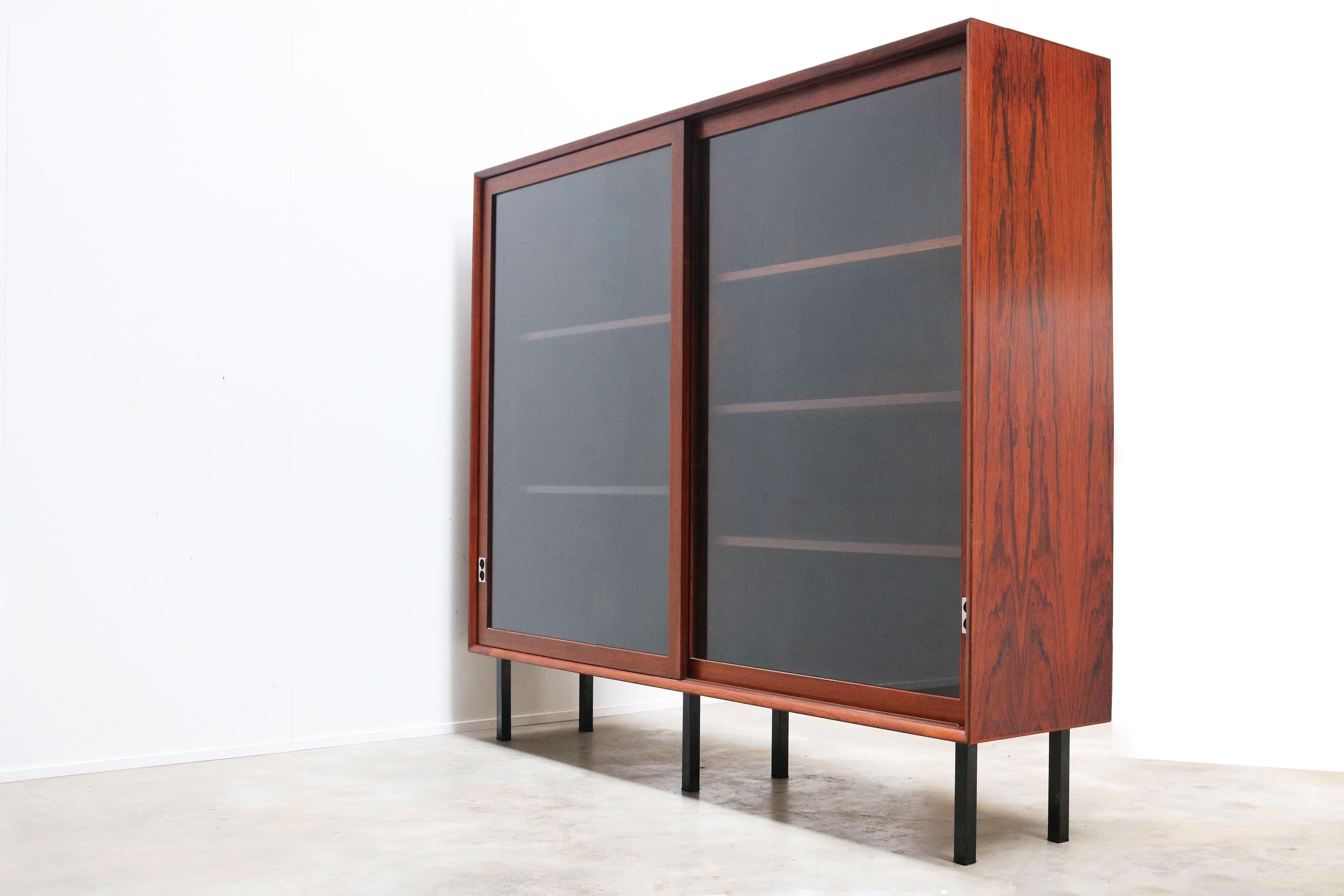Scopri l'apice della raffinatezza moderna di metà secolo con la libreria in palissandro di Arne Vodder, dotata di due ante scorrevoli in vetro con maniglie in alluminio, realizzata nel 1958 per Sibast Furniture. Questo squisito pezzo non è solo una