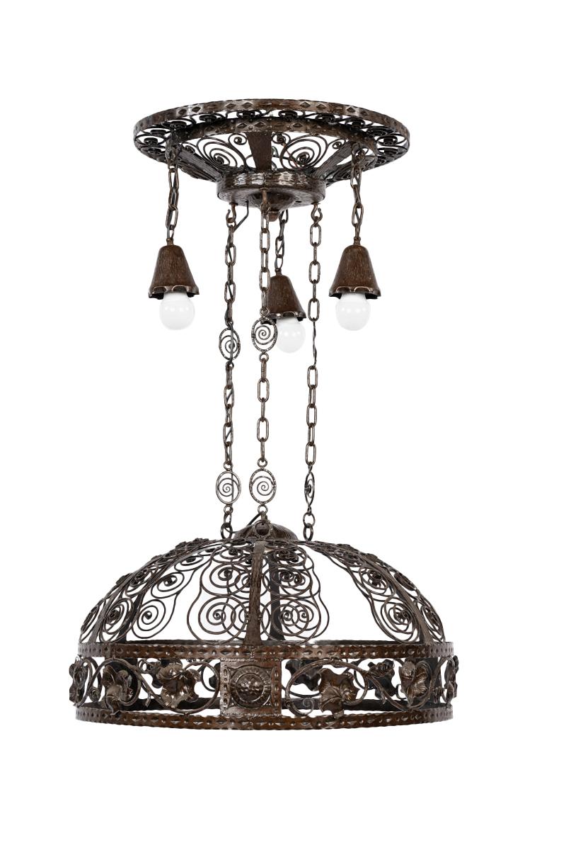 Cette lampe en fer forgé est un exemple étonnant de savoir-faire et de travail artisanal du métal. La lampe présente un dôme rond et ajouré, orné de volutes et de motifs floraux complexes. La structure est reliée à la plaque de plafond par des
