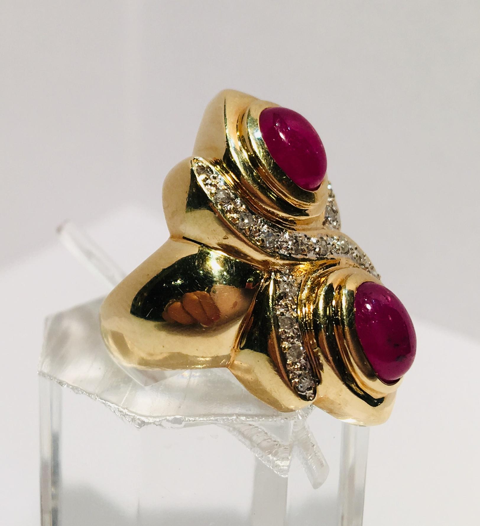 A pair of vivid red ruby oval cabochons are bezel set in 14 karat yellow gold and accented by 22 round brilliant pave set diamonds in a stylized 