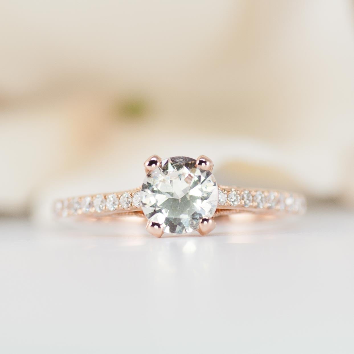 This rose gold engagement ring features a 1.25ct white sapphire as the main center gem--a beautiful alternative to a traditional diamond.

Adding to the art deco design style of the setting are 64 sparkling diamonds on band and sides of the