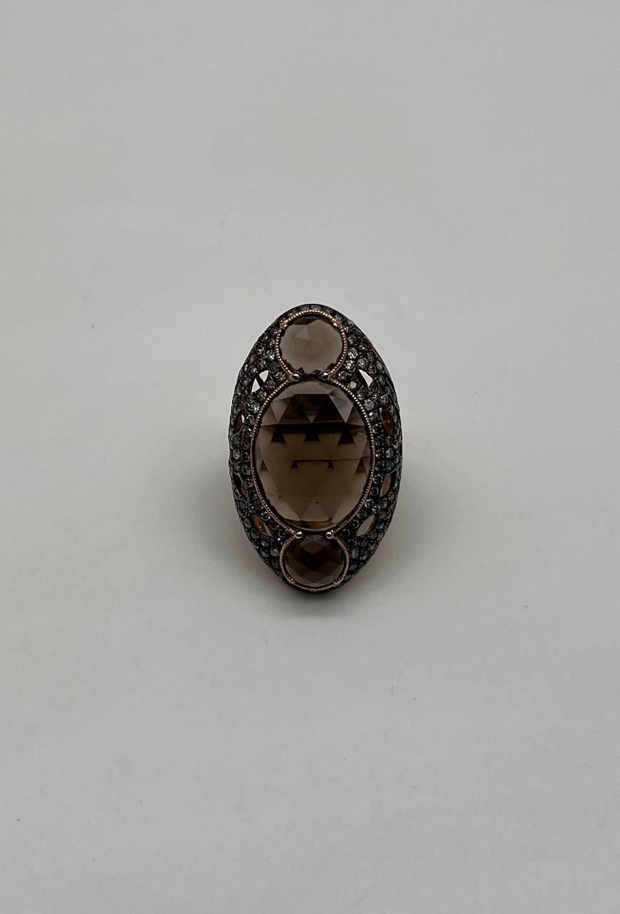This striking ring showcases a large, faceted central brown smoky quartz surrounded by intricate latticework. The setting is crafted from 14k gold, enhancing the warm tones of the stone. Smaller round stones accentuate the top and bottom, adding