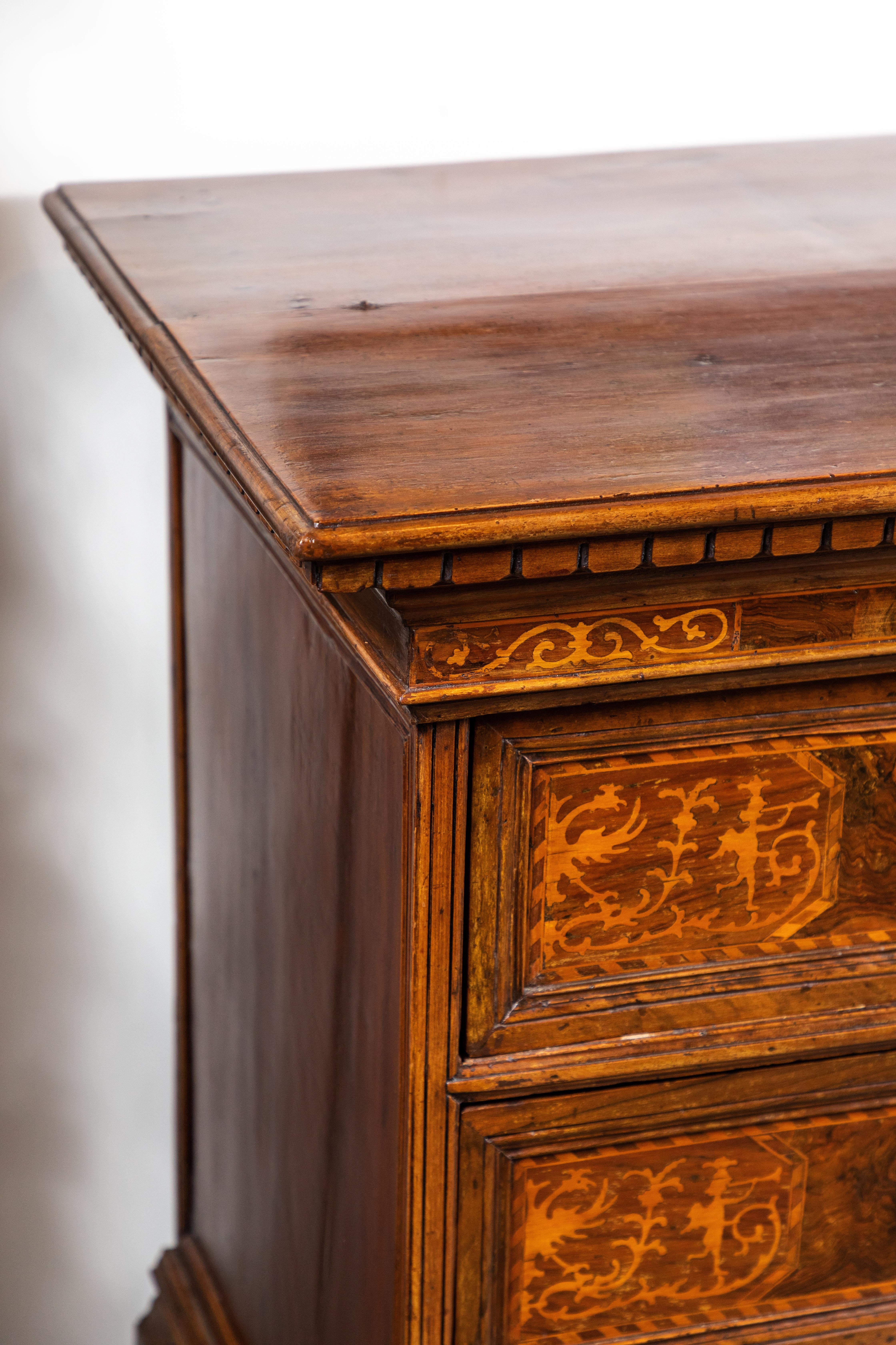 Hand carved and beautifully inlaid, three-drawer, walnut and fruitwood Tuscan commode with a keyed, hinged, flip top. The drawers featuring whimsical scenes of a herald blowing a trumpet, surrounded by foliate scrolls, circa 1820.