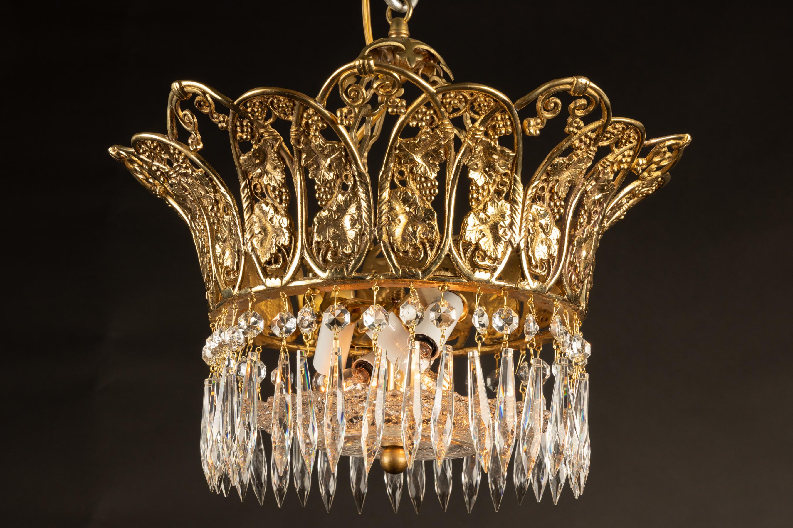 This beautiful early 20th century French chandelier features fantastic crystal work, a beautiful cut crystal center dish, and a delicately ornate crown. The crown features a grape motif, alluding to Bacchus the god of wine. Its bronze glimmers in