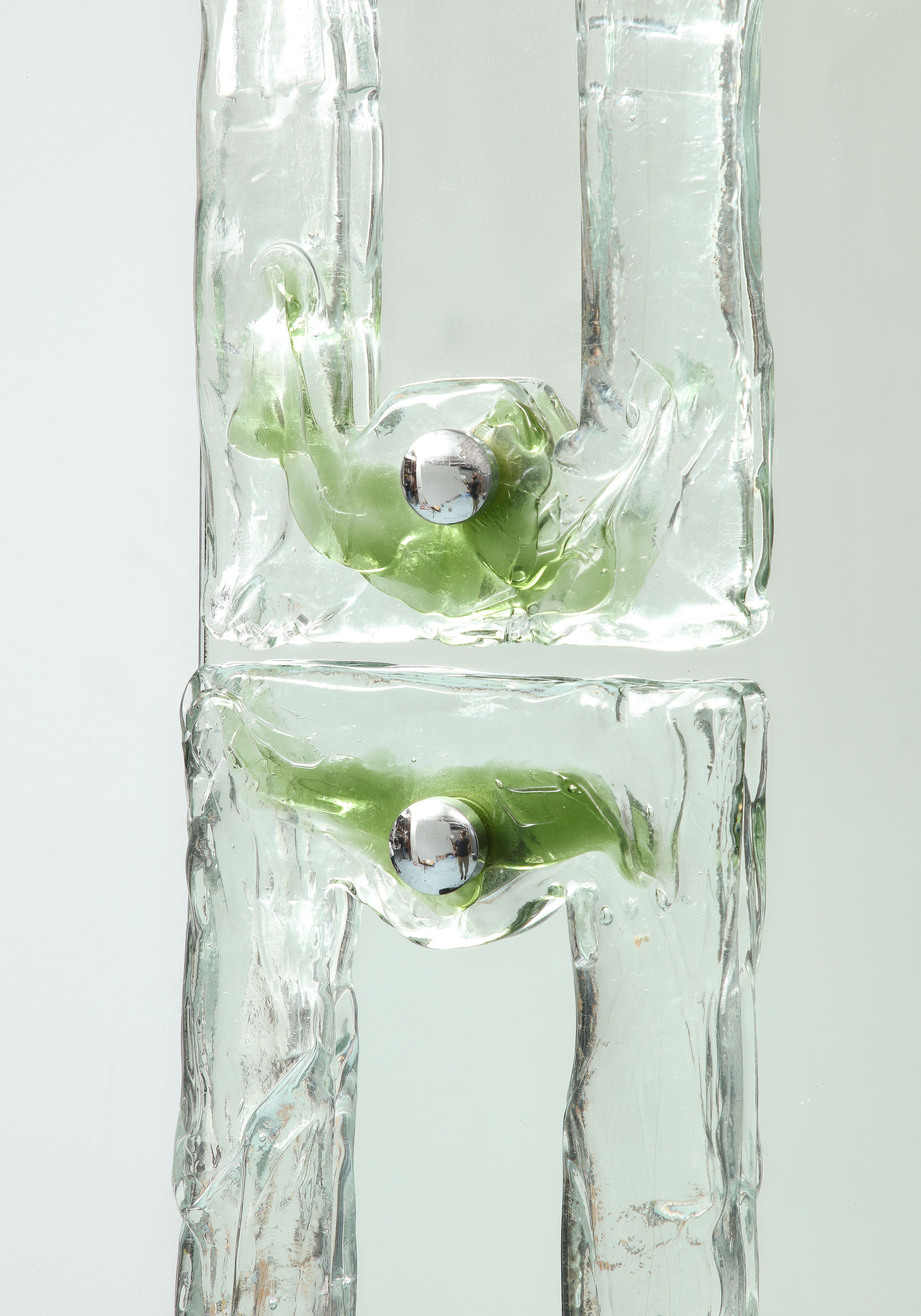 Der ursprünglich für ein Hotel in Neapel entworfene Spiegel besteht aus 4 Elementen aus mundgeblasenem Milchglas, die von Chromknöpfen gehalten werden, auf denen sich grüne Reflexe befinden. 