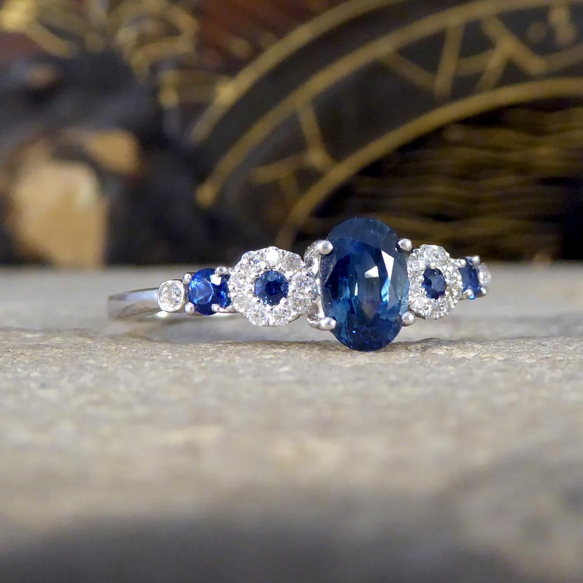 this ring shows a captivating symphony of colour and brilliance all set in 18ct White Gold. At the heart of this extraordinary piece is a resplendent Sapphire, taking centre stage like a star in the night sky. This vibrant gem is flanked by two
