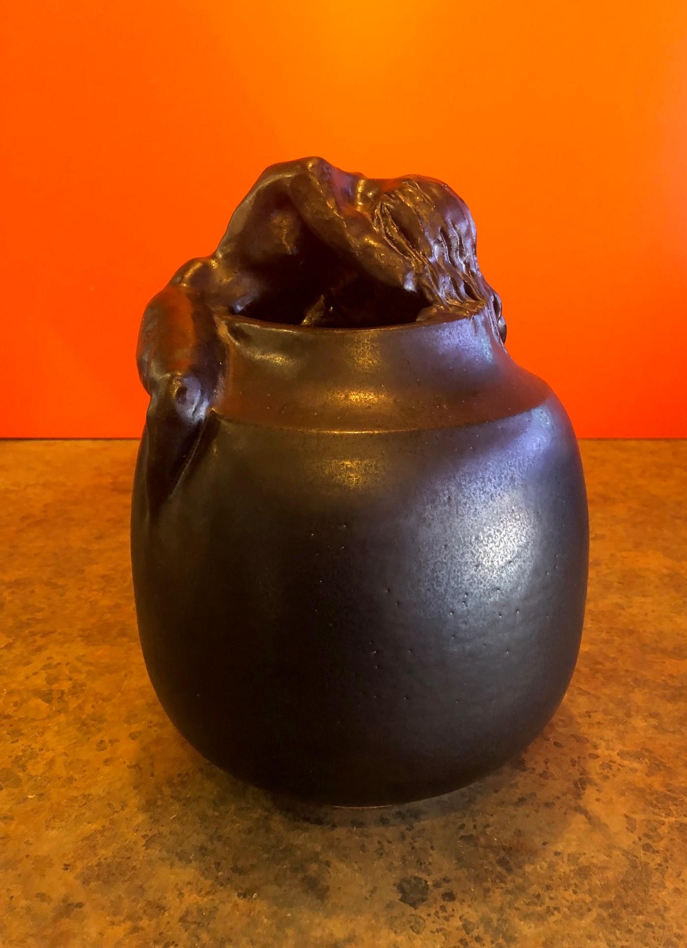 Beautiful hand thrown stoneware pottery vase with nude woman lying on the top ridge, circa 2000. The piece is finished in a matte black glaze and is signed (cannot make out the artists name) and dated on the underside. The piece measures 8