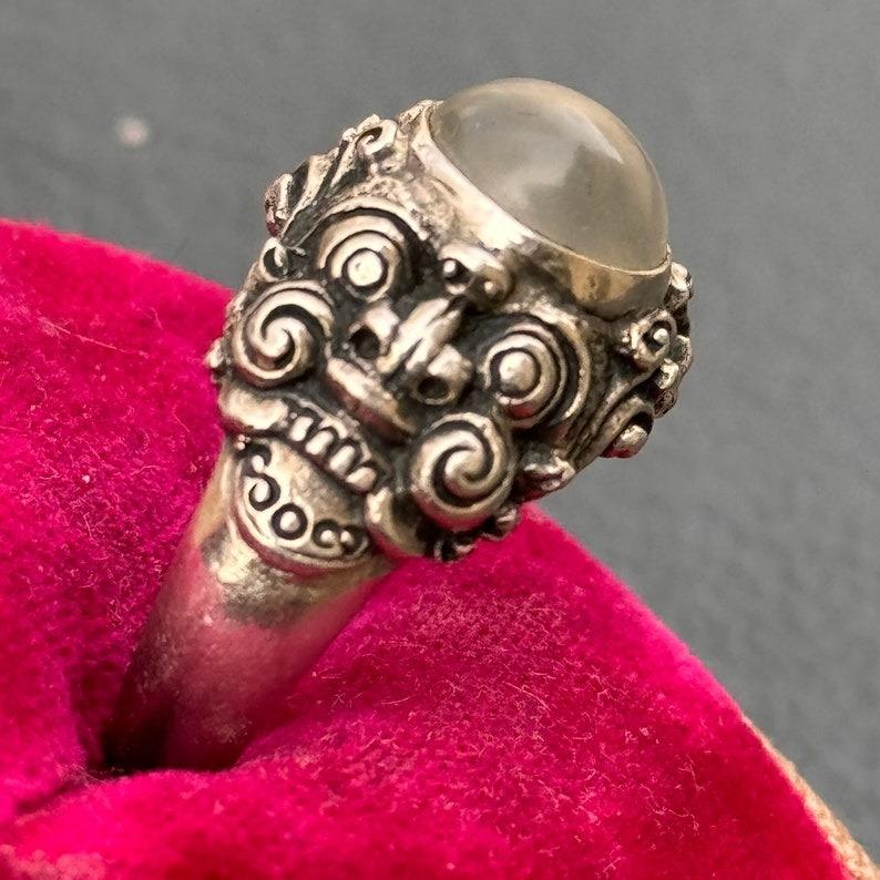 Dieser unverwechselbare Ring zeichnet sich durch ein meisterhaftes Design mit aufwändiger Handwerkskunst aus und zeigt zwei detaillierte Kirtimukha (glorreiche Gesichter), die einen zentralen Mondstein einrahmen. Das Stück ist ein außergewöhnliches