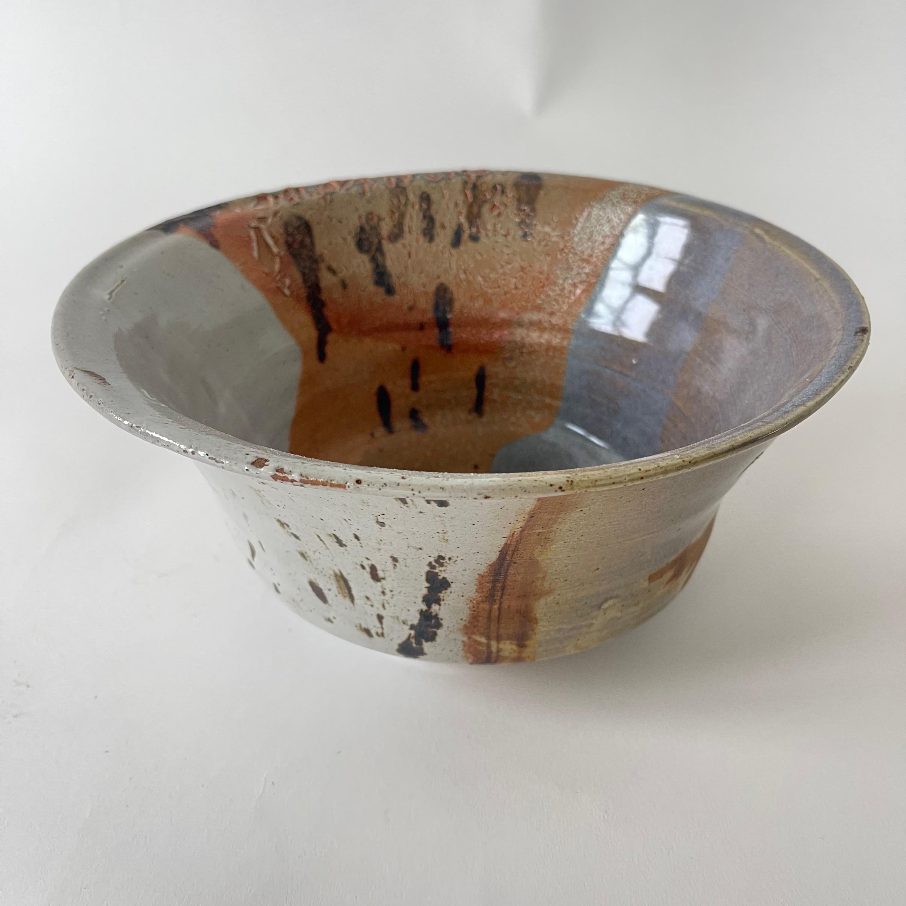 Bol ou plat de service unique en poterie Studio du milieu du siècle, réalisé en argile coulée à la main avec une belle glaçure multicolore vibrante de rouille, orange, bleu, gris et marron, États-Unis, années 1960, marqué ANT sur le fond.