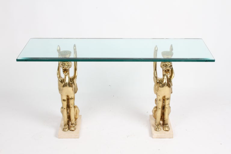 Very unique 1970s Italian Hollywood Regency double pedestal console table or foyer table with two large stylized bronze Griffins mounted to heavy travertine bases that are supporting a thick beveled glass top. Glass is 3/4