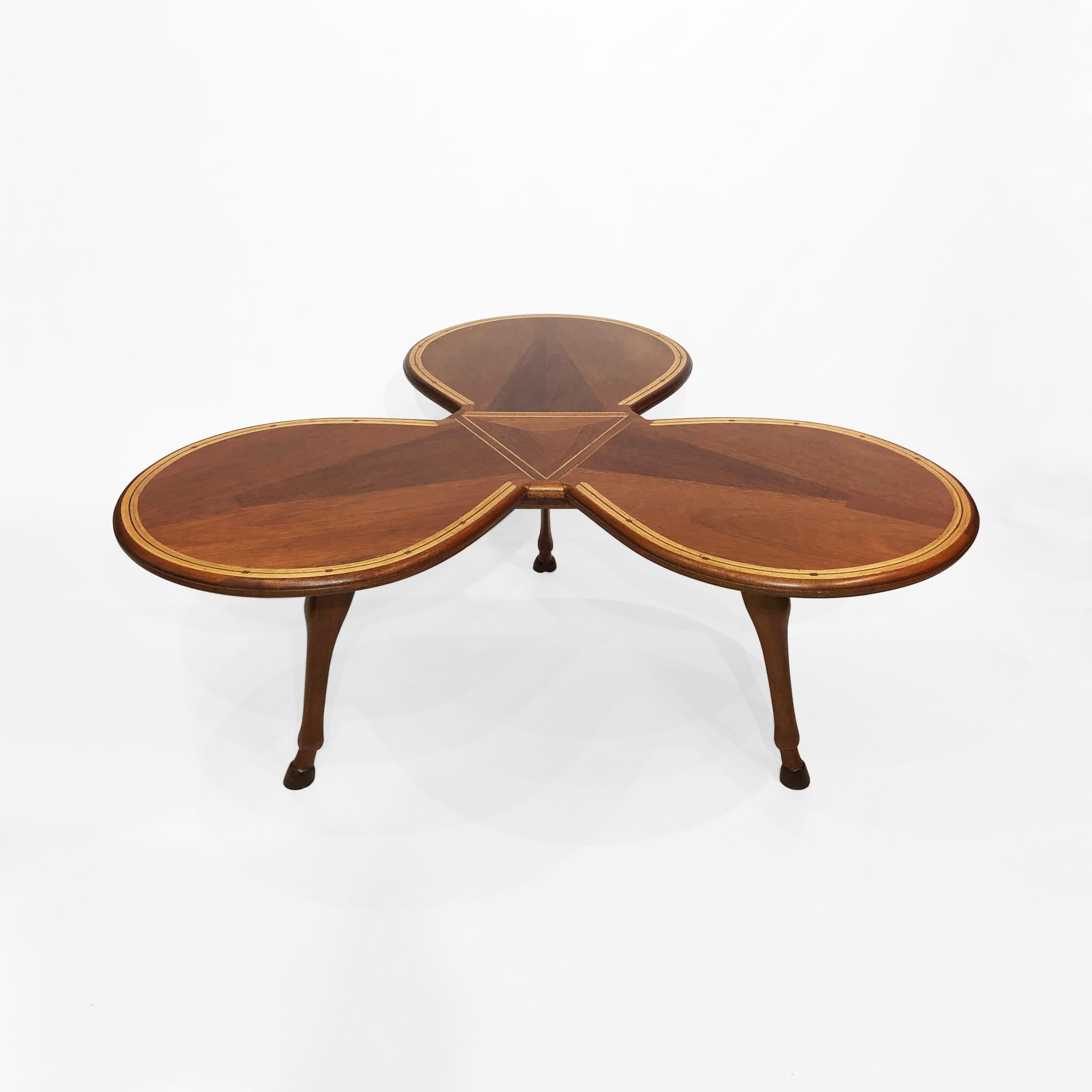 This tripod coffee table in the form of clover leaf and horse petals is a fine example of Midcentury handcrafted marquetry. The three elegant hoof-shaped legs make this coffee table reminiscent of Jacque Adnet’s pieces. The table top is beautifully