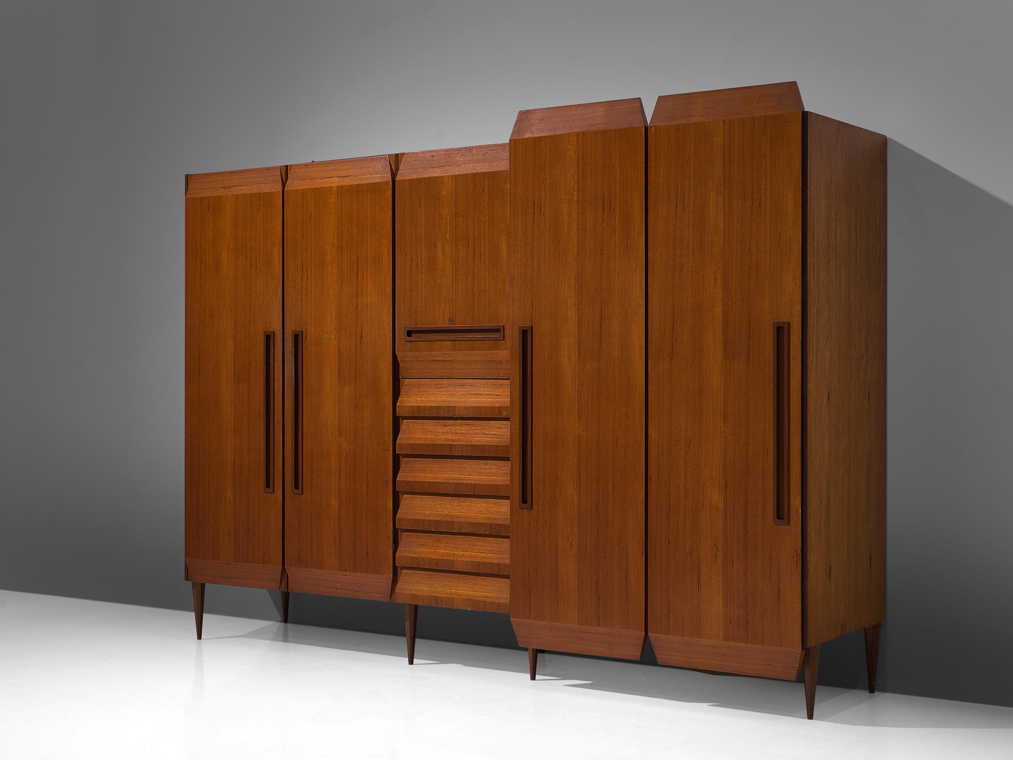 Wardrobe, teak, Italy, 1960s

Italian wardrobe executed in teak. Four doors and a colum with drawers structure this wardrobe which features two levels as two outer doors are deeper and higher than the rest of the wardrobe. The appearance is unique