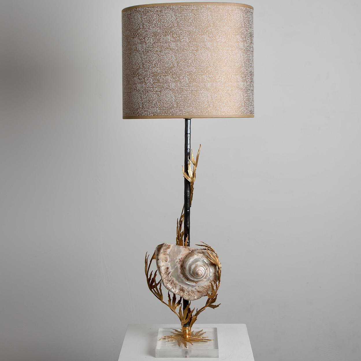Une lampe de table unique avec un grand véritable coquillage sur la base. La lampe est ornée de magnifiques détails en corail en laiton et est livrée avec un abat-jour semi-éclatant fait à la main qui donne une lumière chaude.
La lampe est