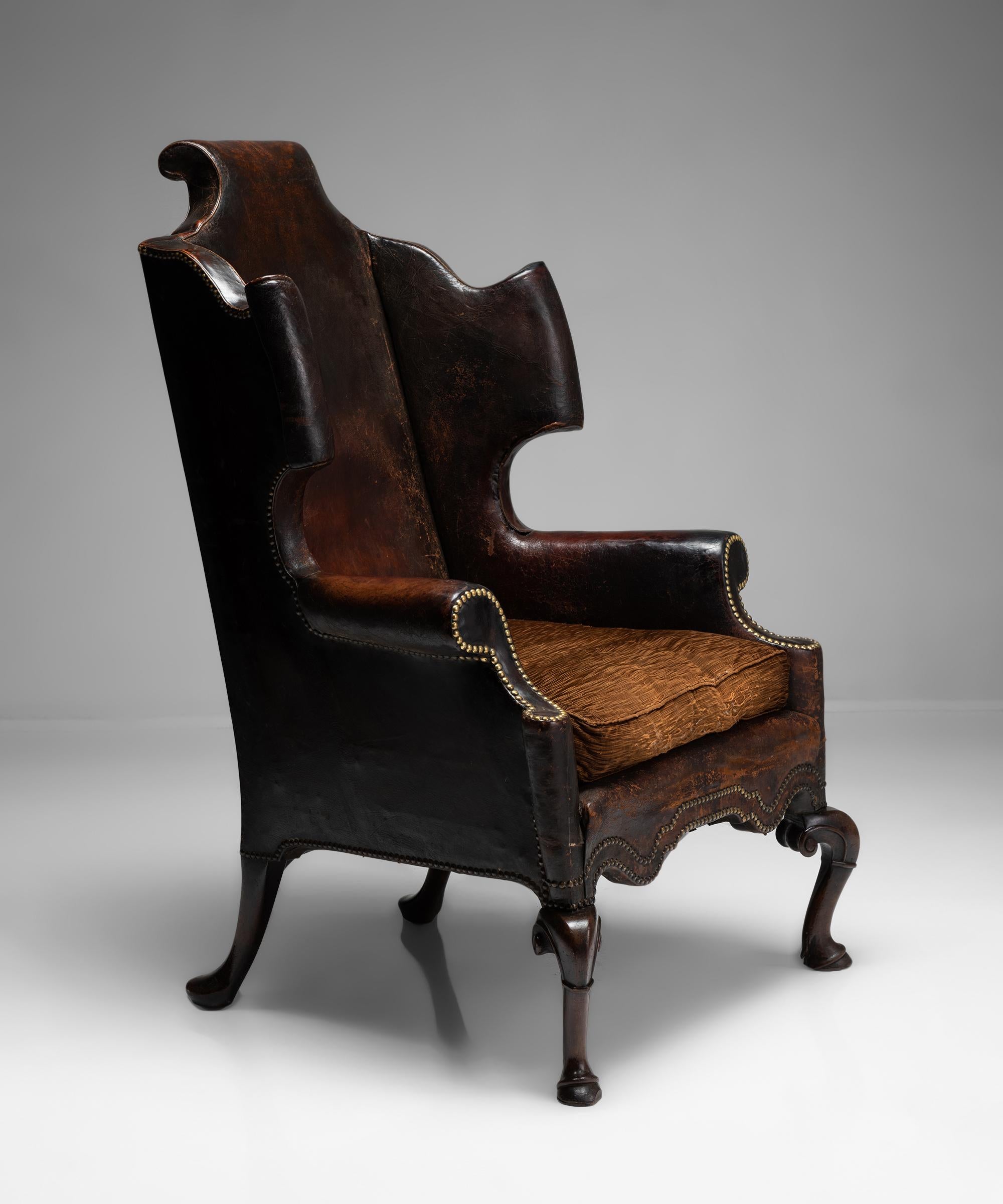 
William & Mary period leather wing chair on raised walnut cabriole leg with hoof and fetlock details and original leather upholstery.