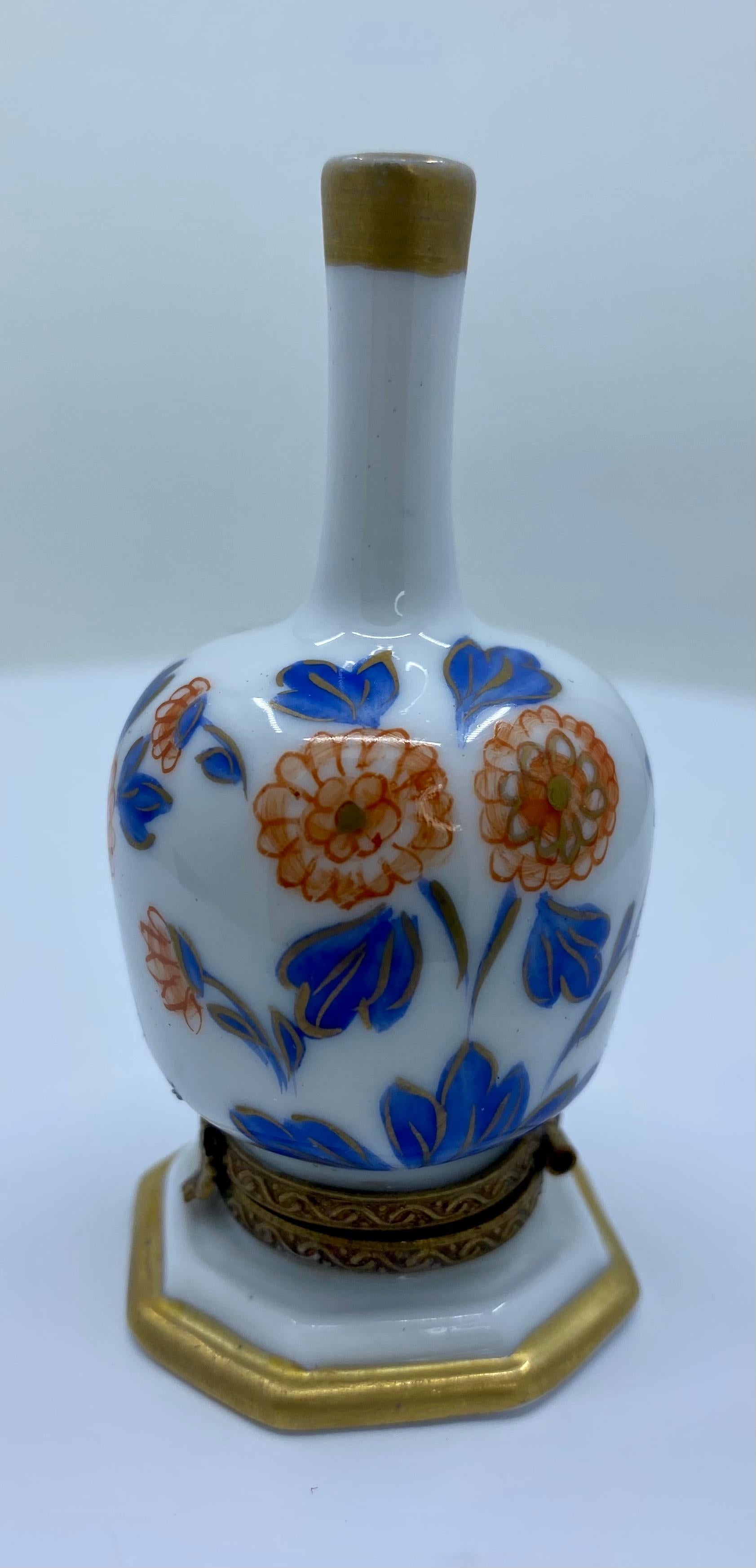 Collectible and very unique, Limoges porcelain miniature trinket box is handmade and hand painted in France. It features beautiful blue and orange tone flowers and leaves with touches of gold covering the long neck vase shaped box. Accenting the box