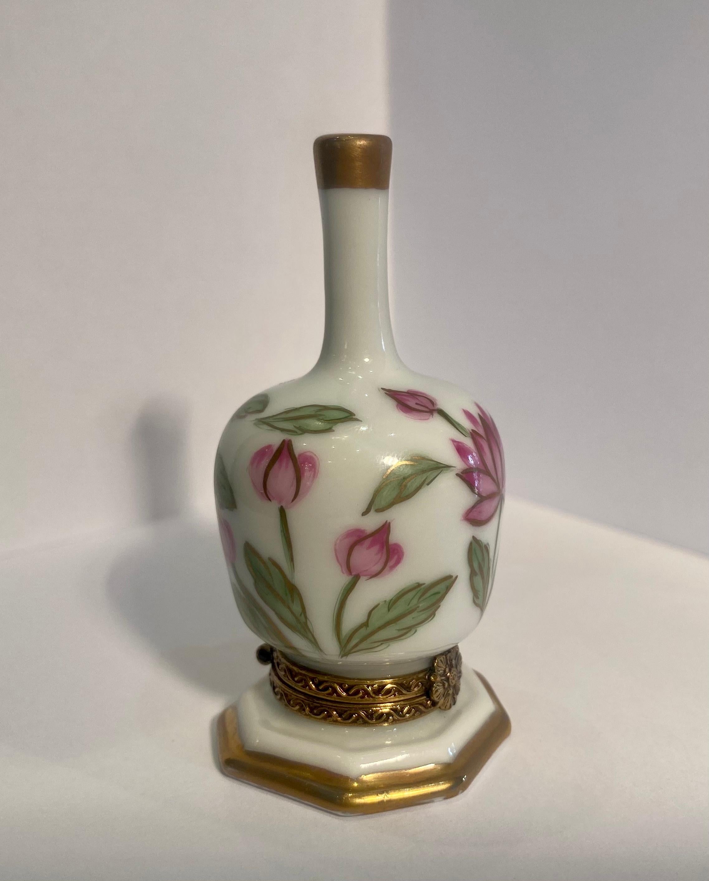 Collectible and very unique, Limoges porcelain miniature trinket box is handmade and hand painted in France and features beautiful multicolored pink tone lotus style flowers on the long neck vase shaped box. Accenting the box on the top of the neck