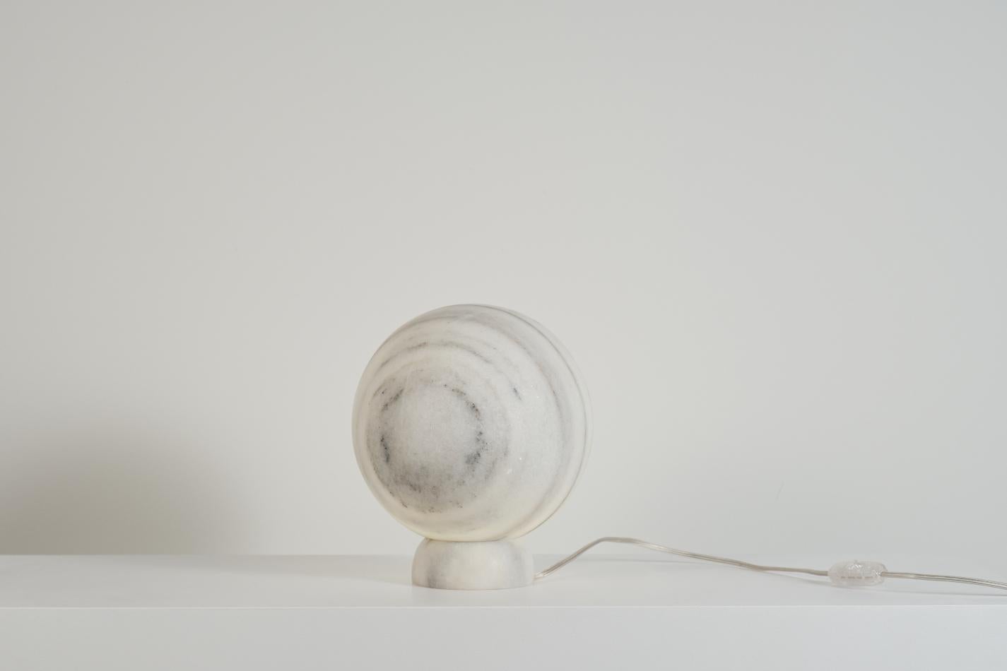 Handcarved Makrana Marble warm light table lamp Nearness III 'Moonlight' by designer Alba Abiad with Naveen Jose. Creates a calm and relaxing atmosphere in space. 
Carved out from a single piece of marble, handpicked and handcrafted, the light