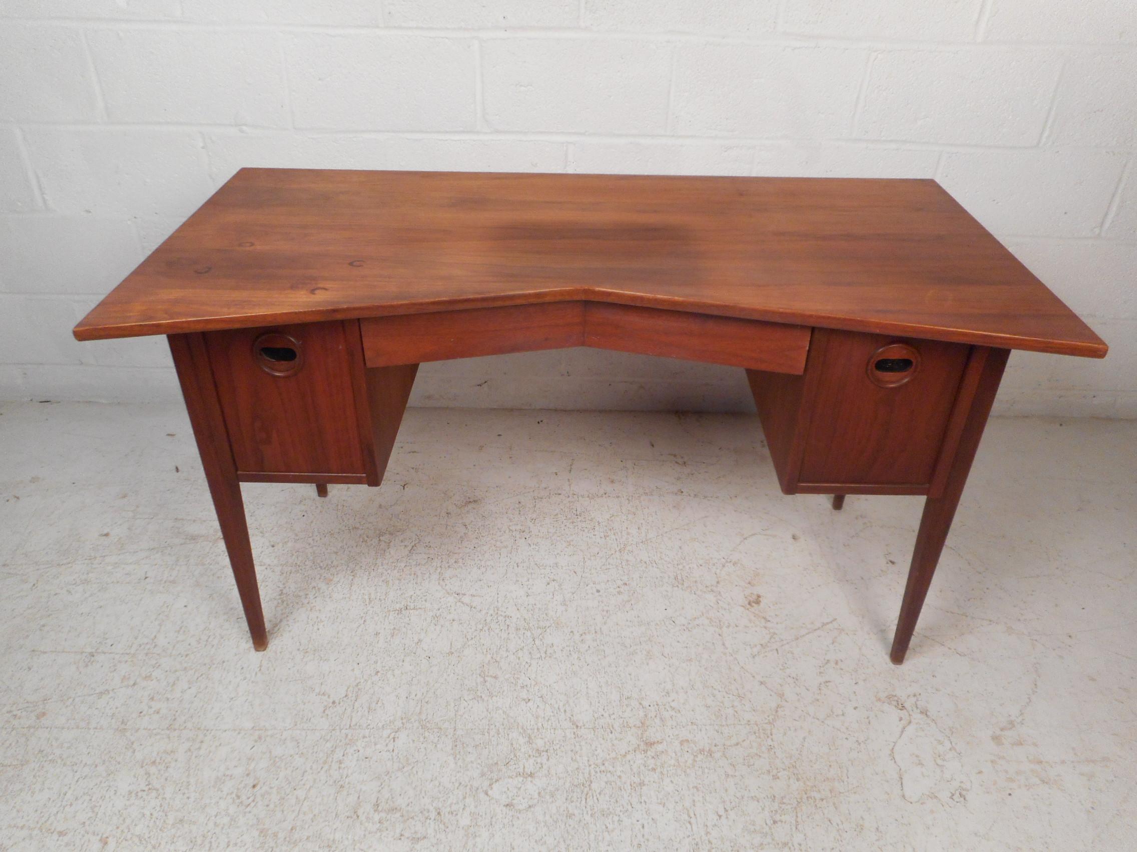 Stylish and unusual midcentury desk. An angular desk front and drawer give this piece a very unique look. A pair of oversized drawers on either side of the desk offer ample storage/filing space. A panel of woven cane adorns the back of the desk