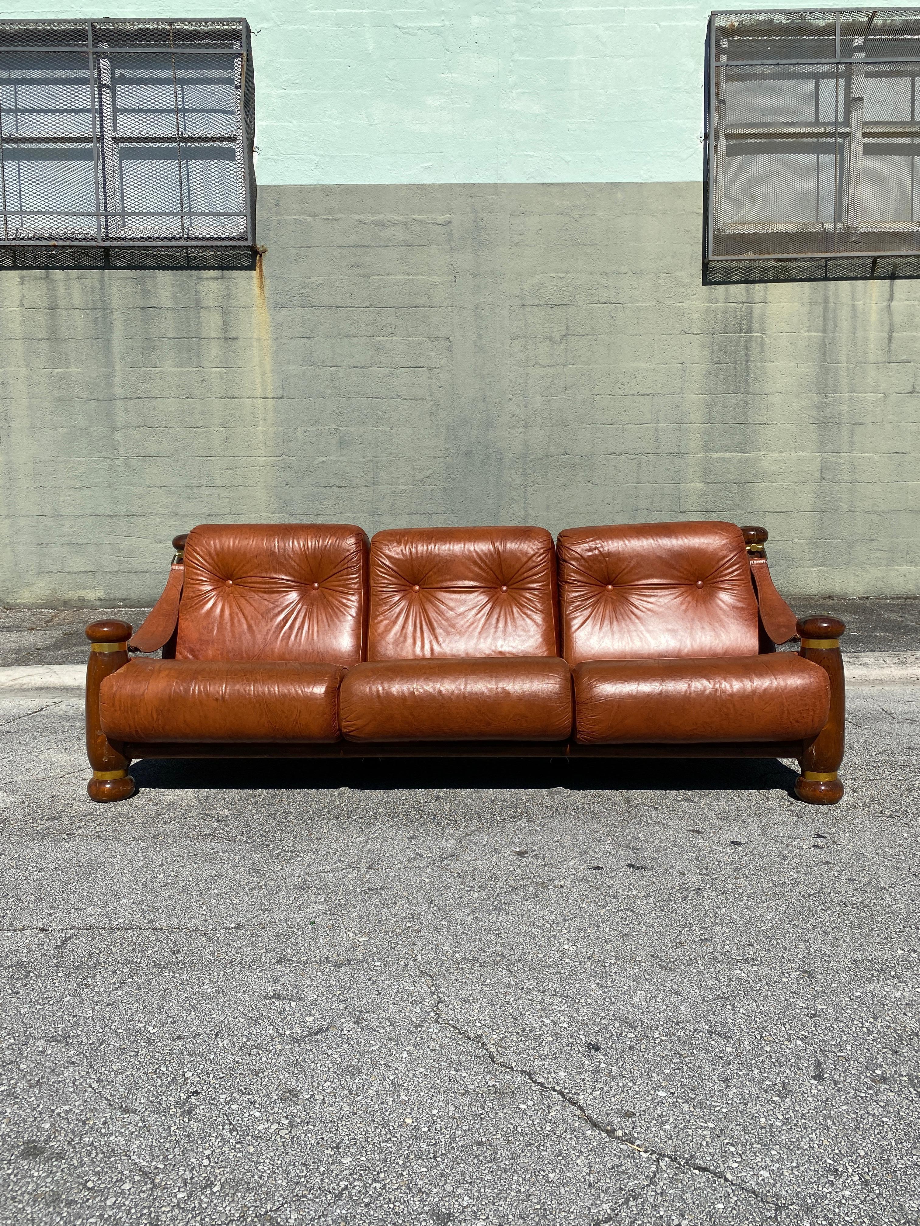 Vintage three seater sofa with pillar arm frames, leather swag armrests complement burnt orange leather cushions.

Circa 1960s.

Measures: 84”W x 37”D x 32”H x 14”SH