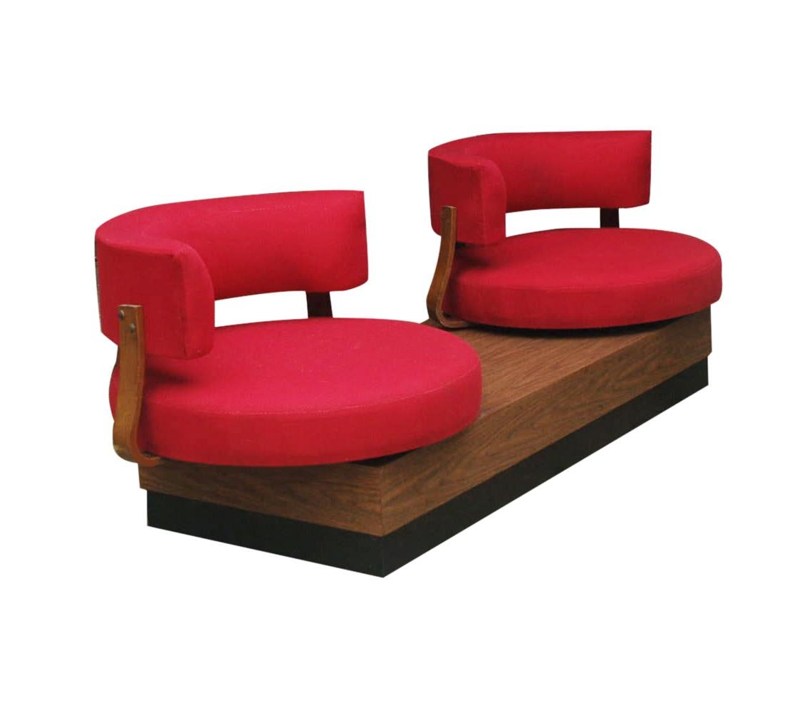 An unusual design from the 1970s. It features a platform base with swiveling barrel back lounge chairs in red upholstery.