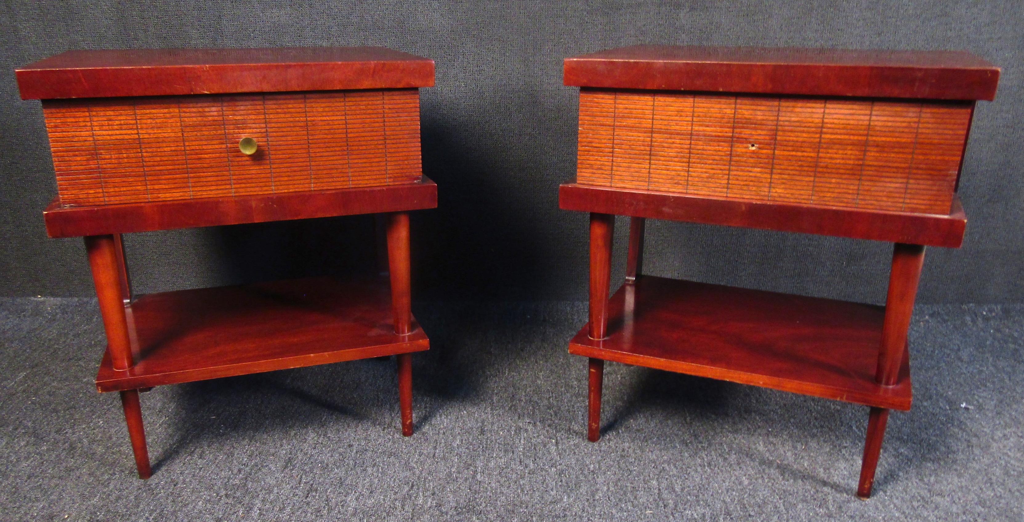 Beautiful vintage modern wood side tables. Each side table features a spacious drawer and shelf below. The drawers are carved in a unique etched grid pattern, encased within a shell of rich red wood, on tapered legs.

Please confirm item location