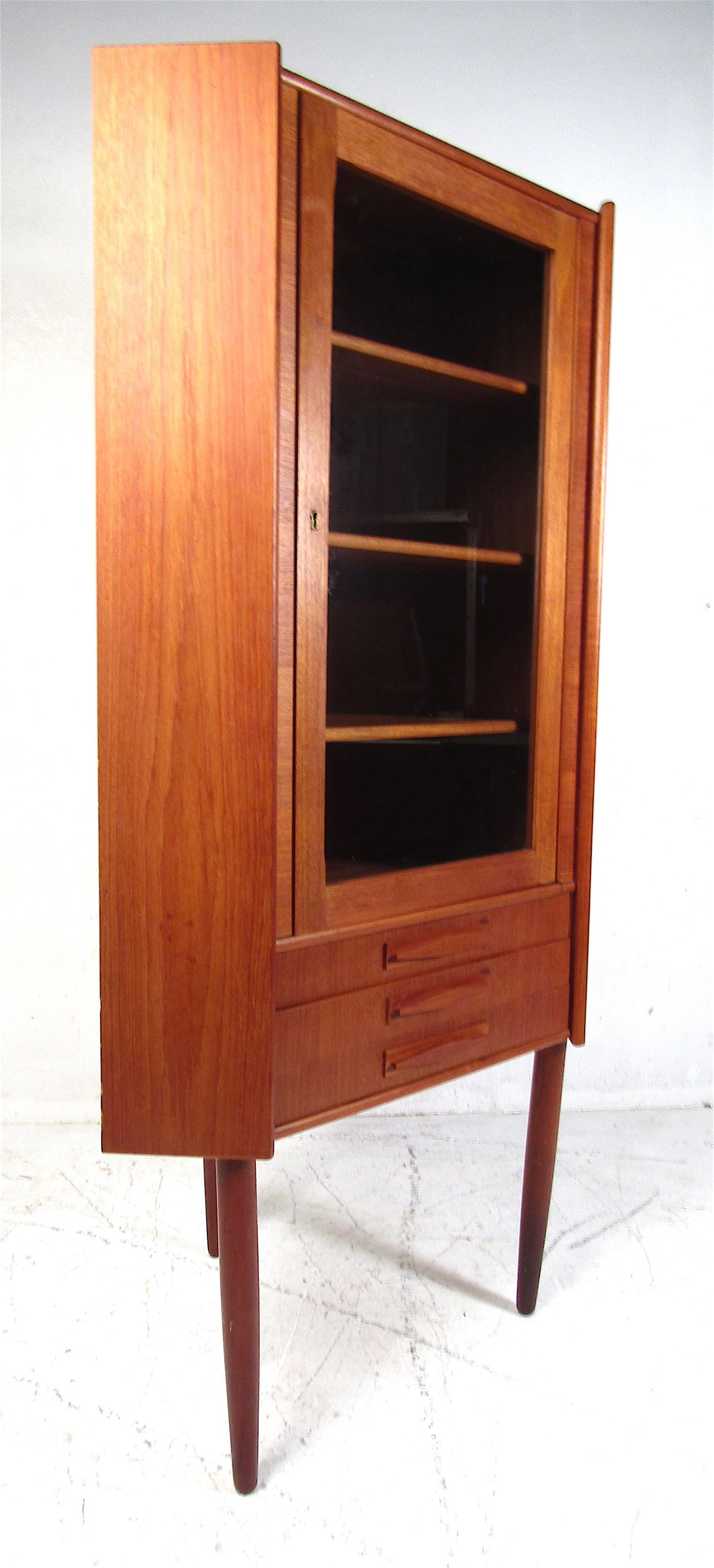 This stunning vintage modern Danish corner cabinet features three shelves and three small drawers on the base. An unusual design that can fit comfortably in any corner of the room. A glass-front cabinet door allows this to function as a display